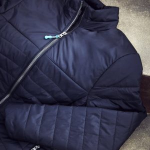A navy puffer jacket featuring a zip closure and a contrasting zipper pull, displayed on a textured surface.