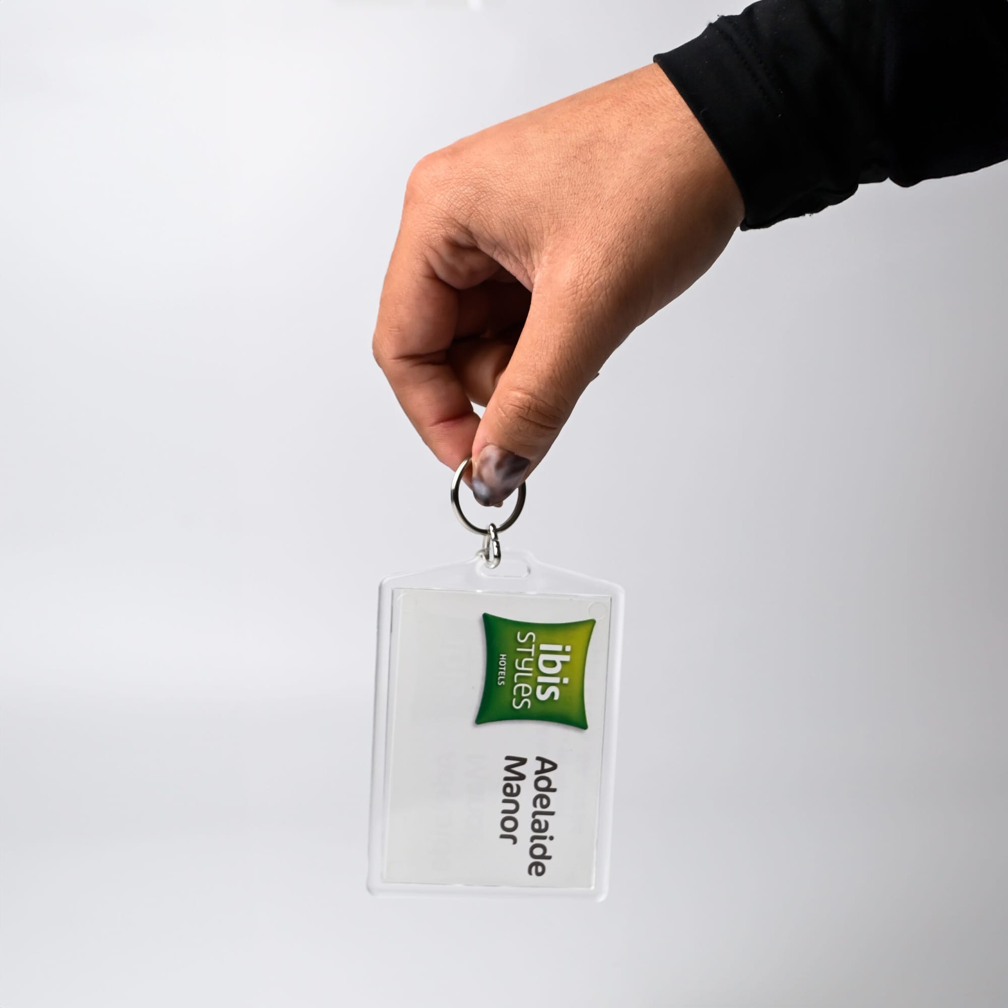 A hand holds a clear hotel keychain with a logo and a tag reading 