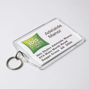 A clear hotel keychain with a ring, featuring green and white branding and a printed address. Australian made.