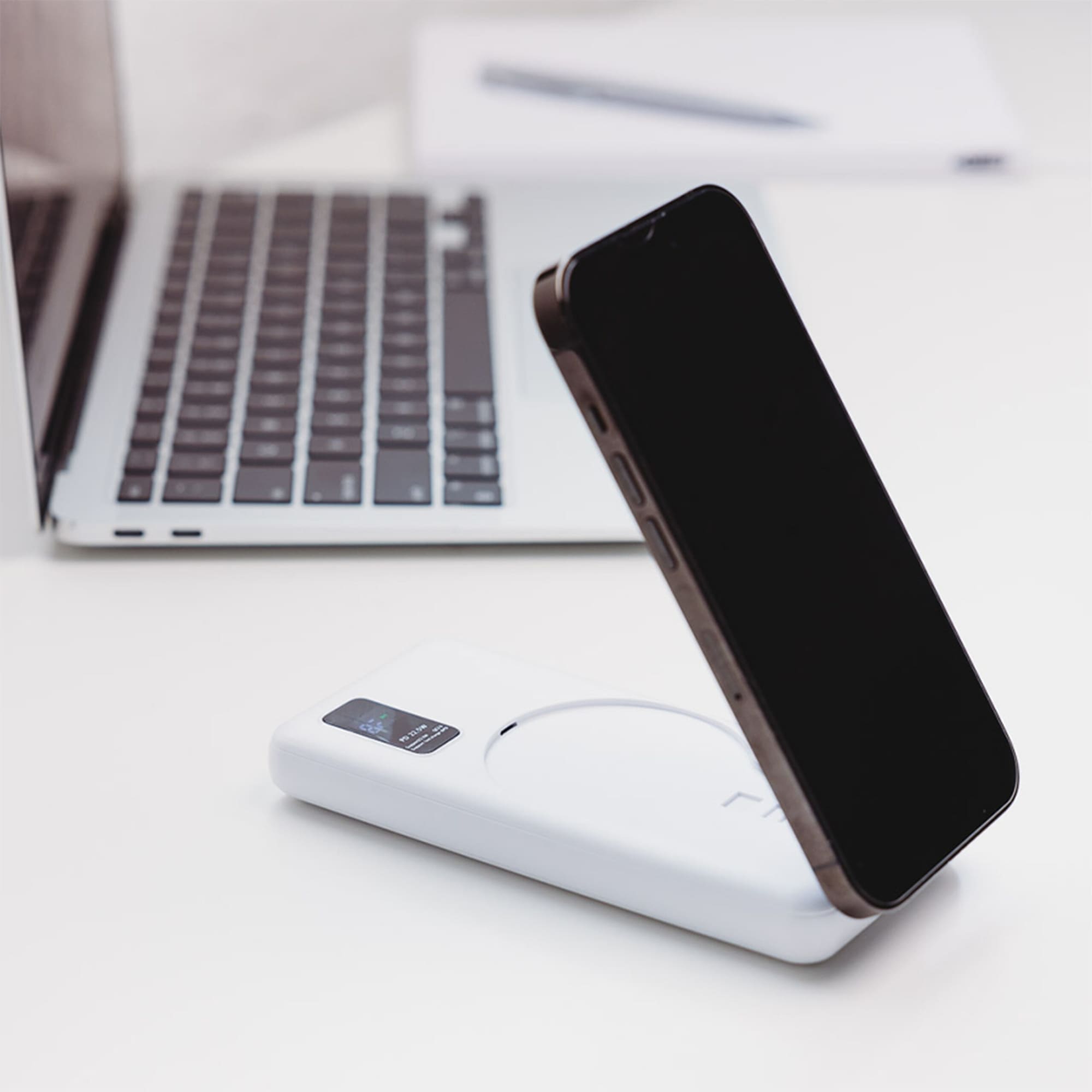 A white power bank with a wireless charging feature and a smartphone in the process of being charged.