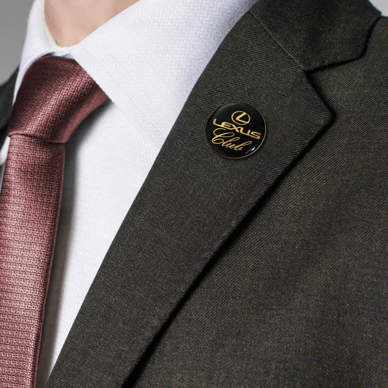 A lapel pin displayed on a dark green jacket, featuring a circular design with a gold logo.