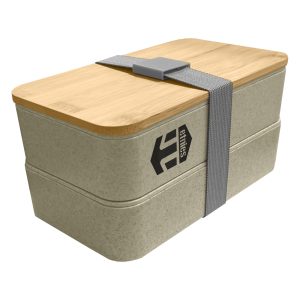 A two-tier wheat straw lunch box in a light beige colour with a bamboo lid and grey strap. Features a logo.