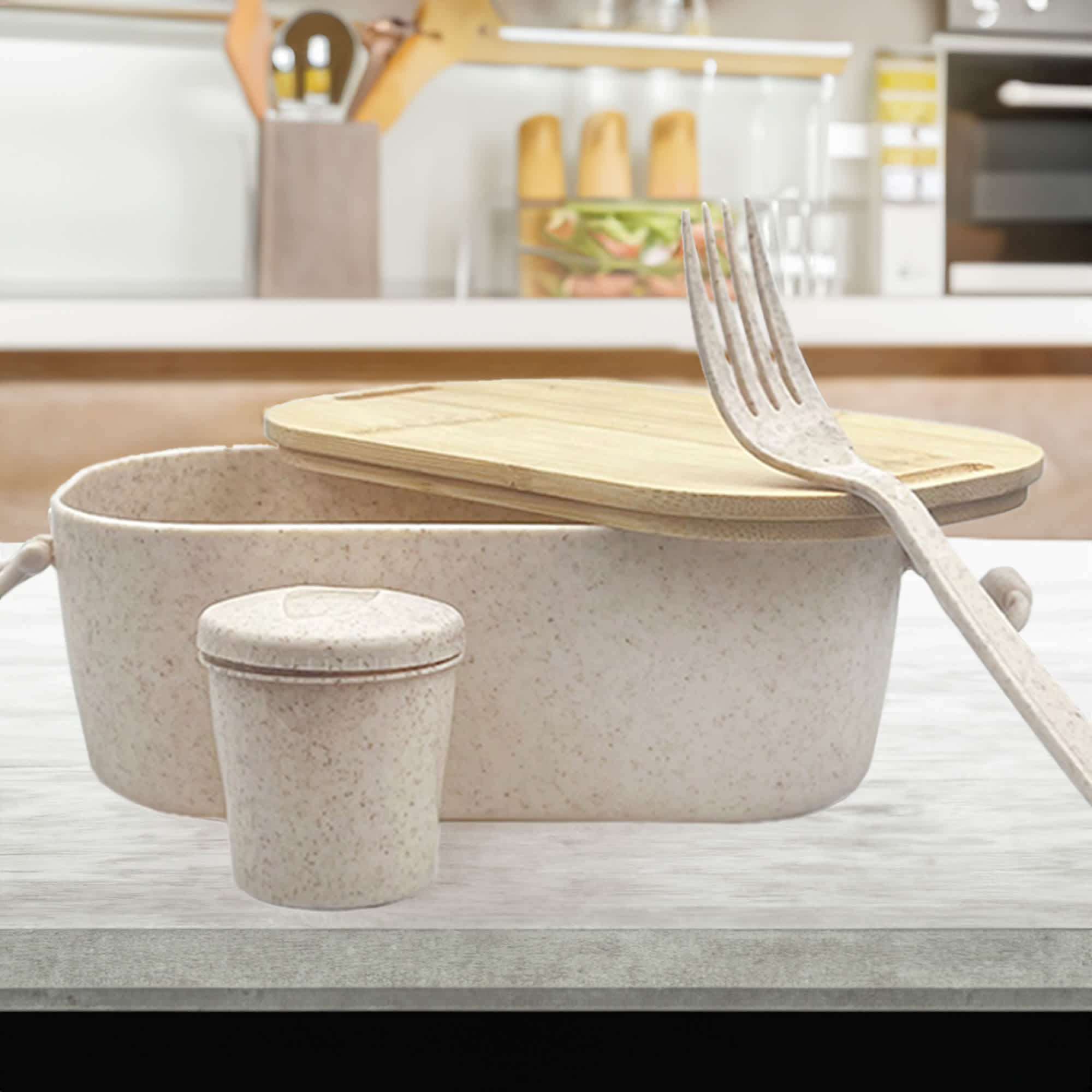 A bamboo lunch box with a light pink hue, accompanied by a small container and a fork, set on a kitchen countertop.