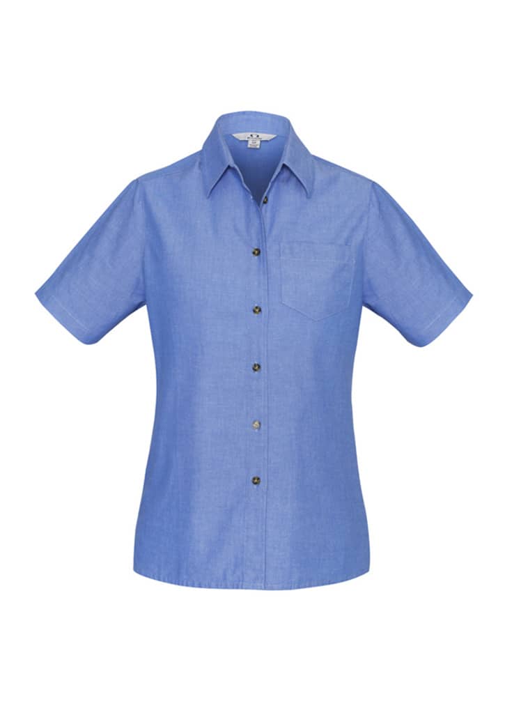A blue chambray short sleeve button-up shirt with a front pocket and button detailing. It has a logo on the label.