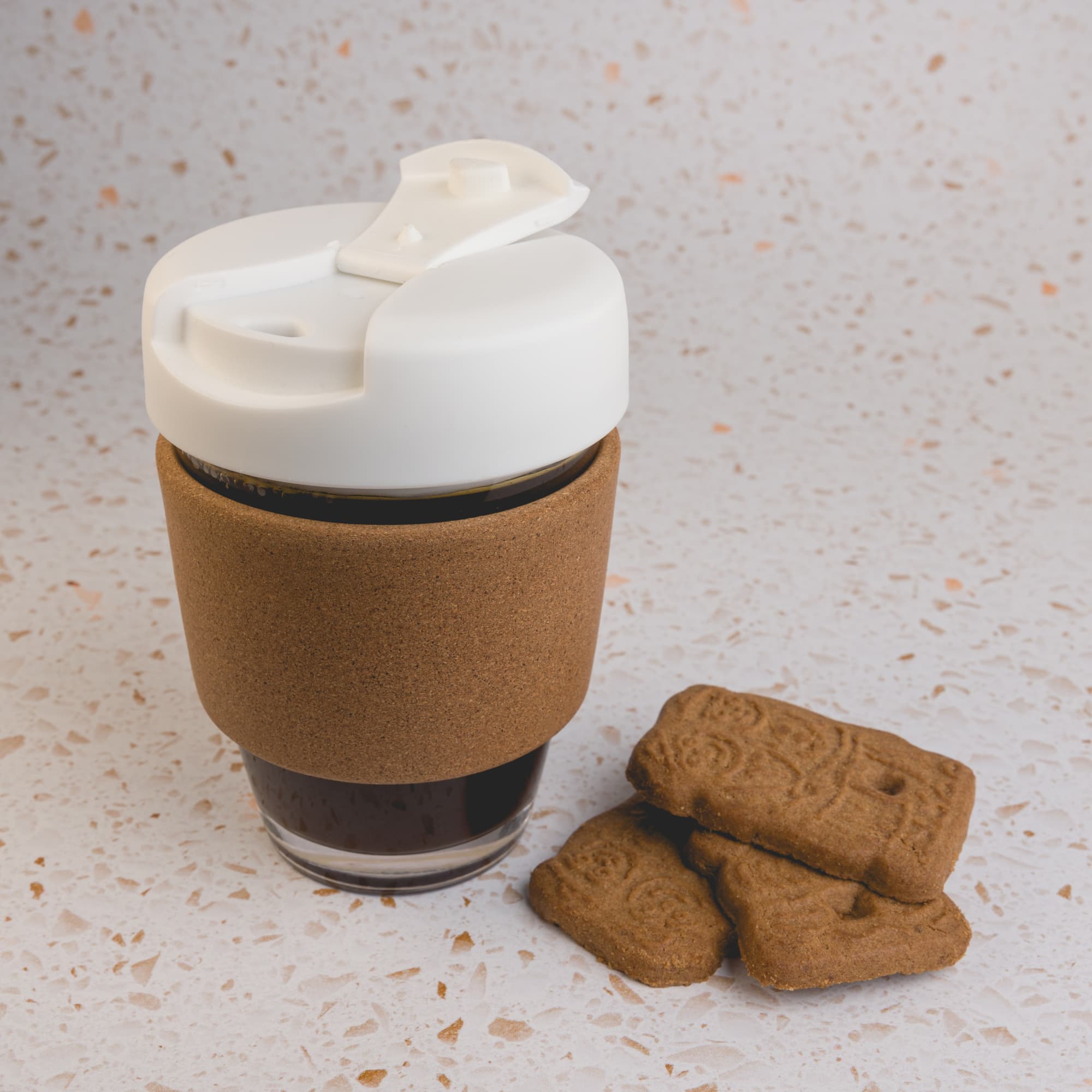 A reusable coffee cup with a cork band and a white lid, accompanied by cookies.