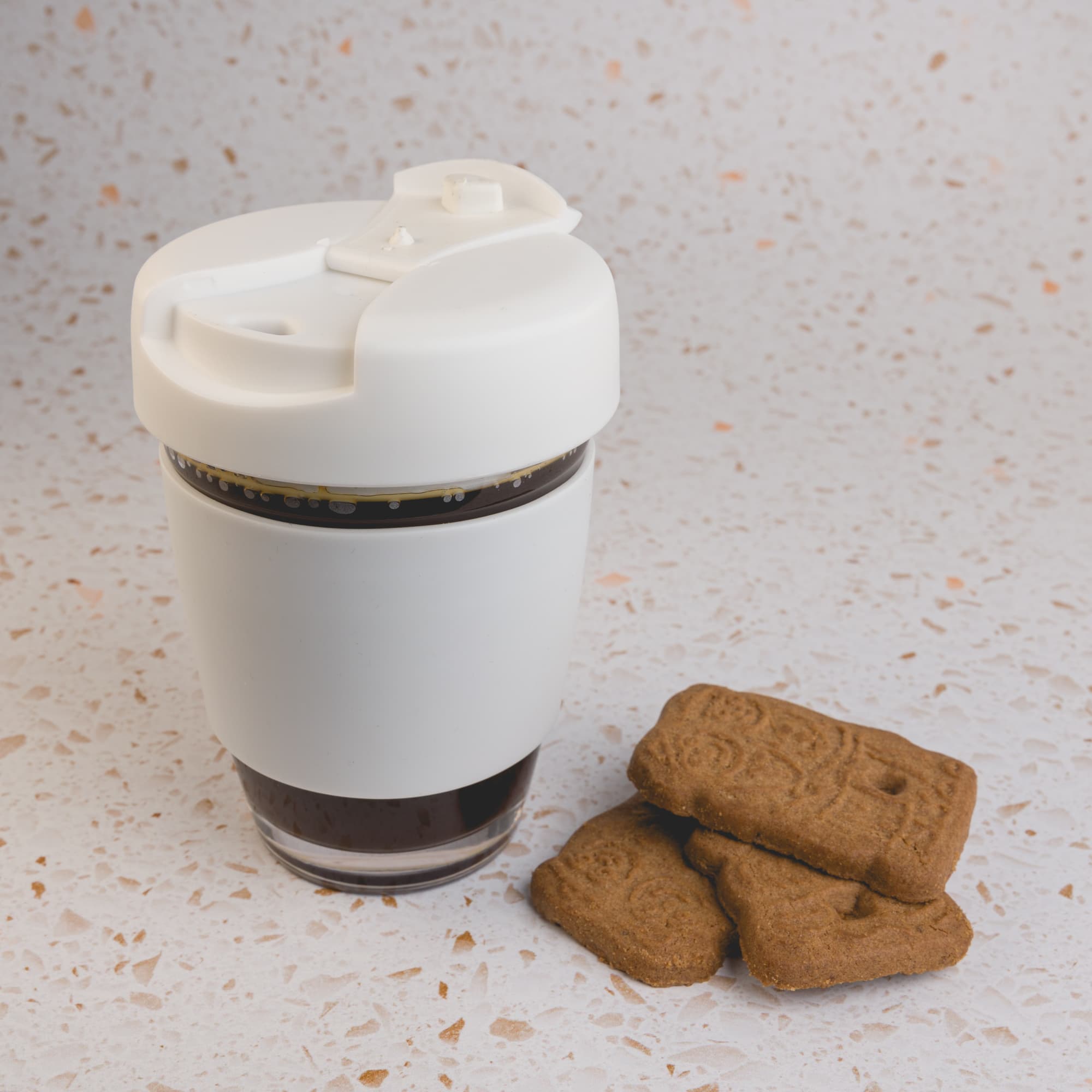 A reusable coffee cup with a flip lid, designed for beverages, accompanied by three biscuit cookies.