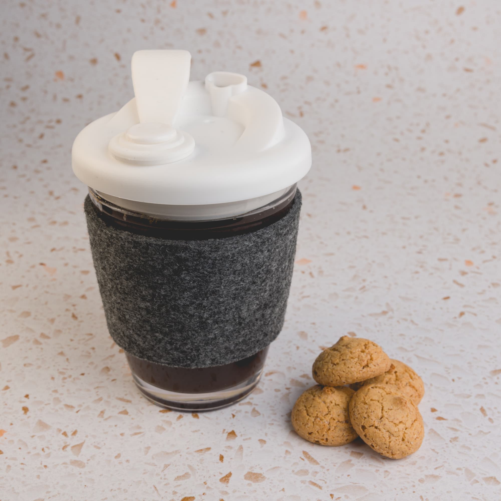 A reusable coffee cup with a snap lid and a dark grey RPET band, accompanied by three small cookies.