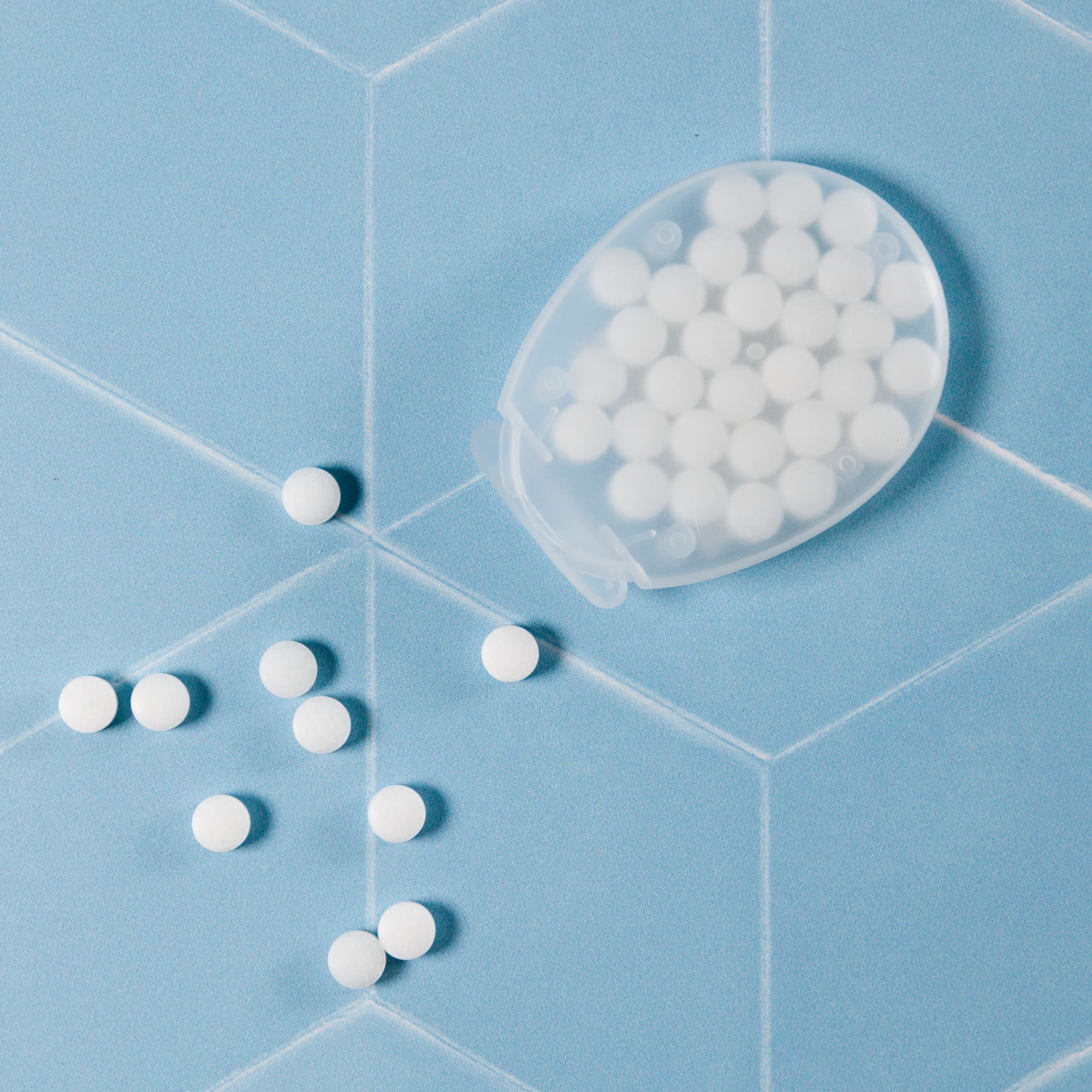 An egg-shaped container filled with white, sugar-free breath mints, with some mints scattered around it.