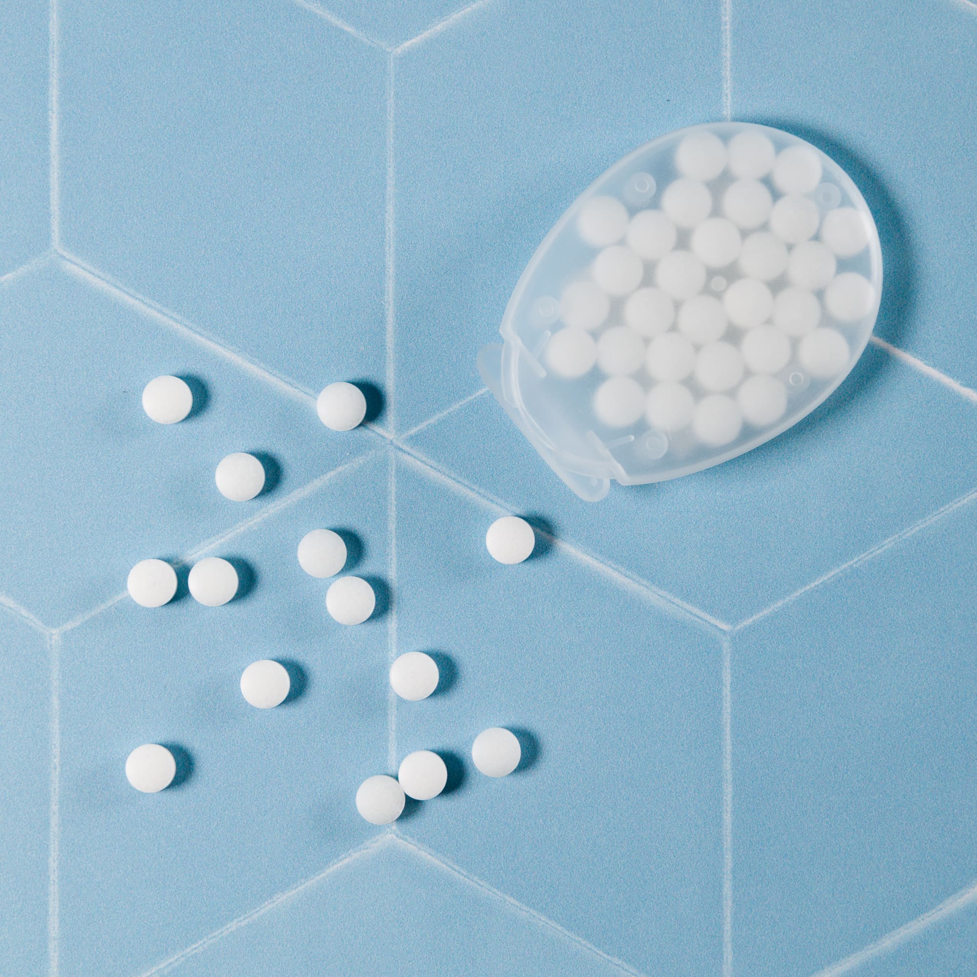 An egg-shaped container of sugar-free breath mints, with several mints scattered around on a blue hexagonal surface.