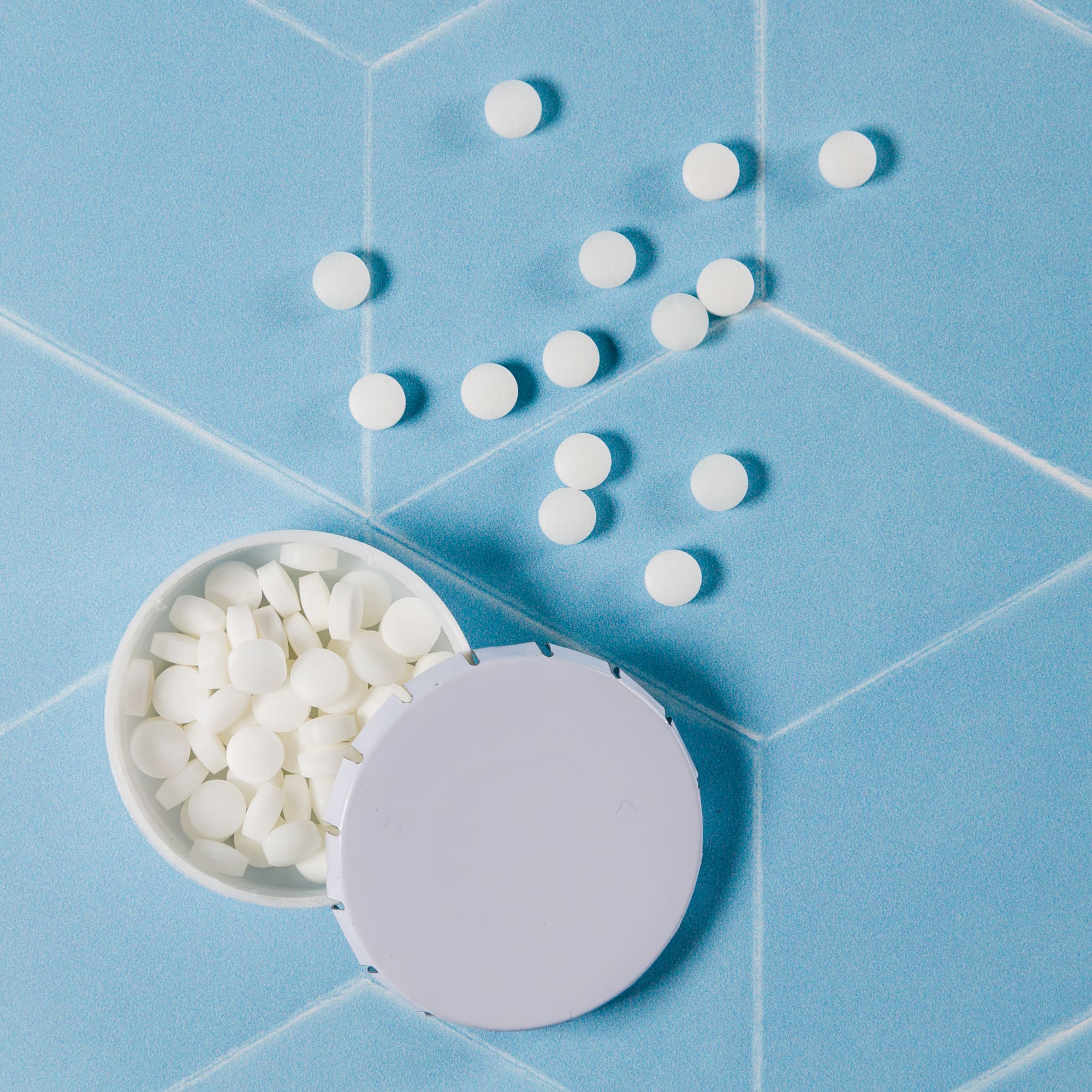 A bowl filled with white mint tablets is placed on a blue surface, alongside several scattered mint tablets.