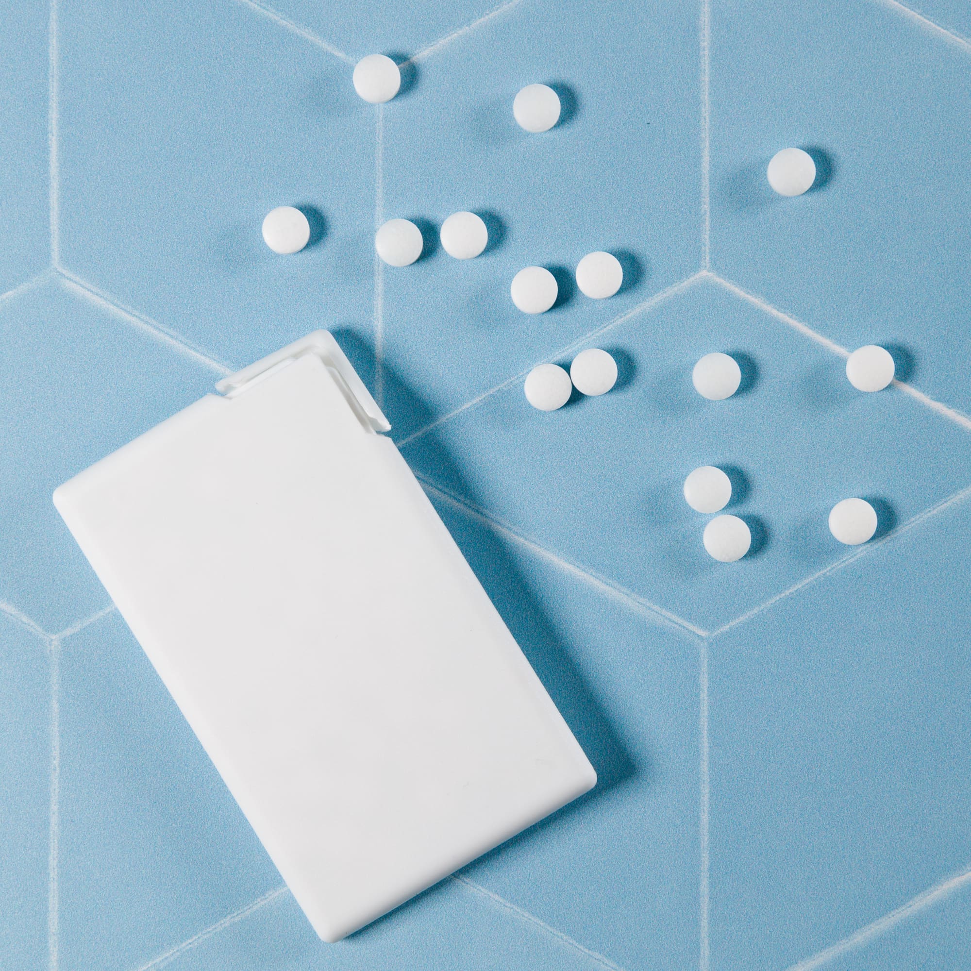 A rectangular container of sugar-free breath mints with several mints scattered around it.