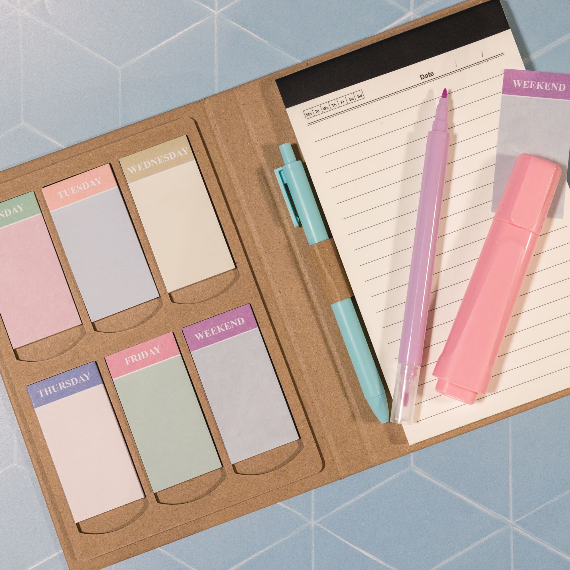 A planner featuring pastel-colored sticky notes and a pen, with a kraft cover and a grid-patterned background.