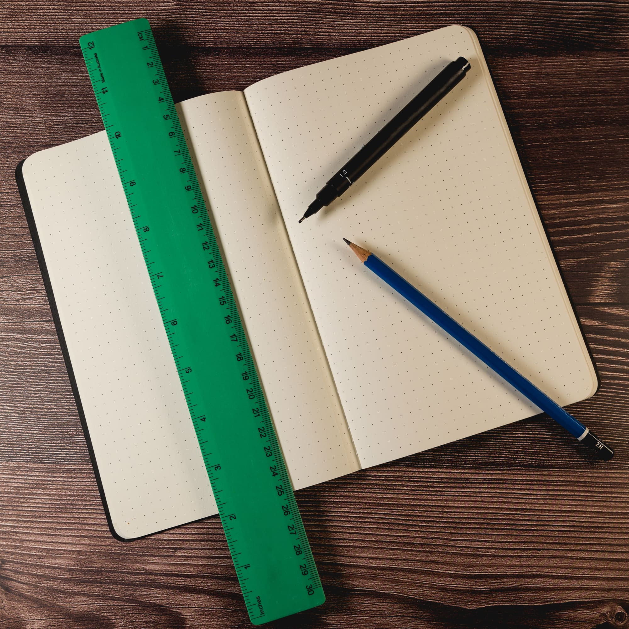 A green 30cm recycled plastic ruler lies on an open notebook with a black pen and blue pencil beside it.