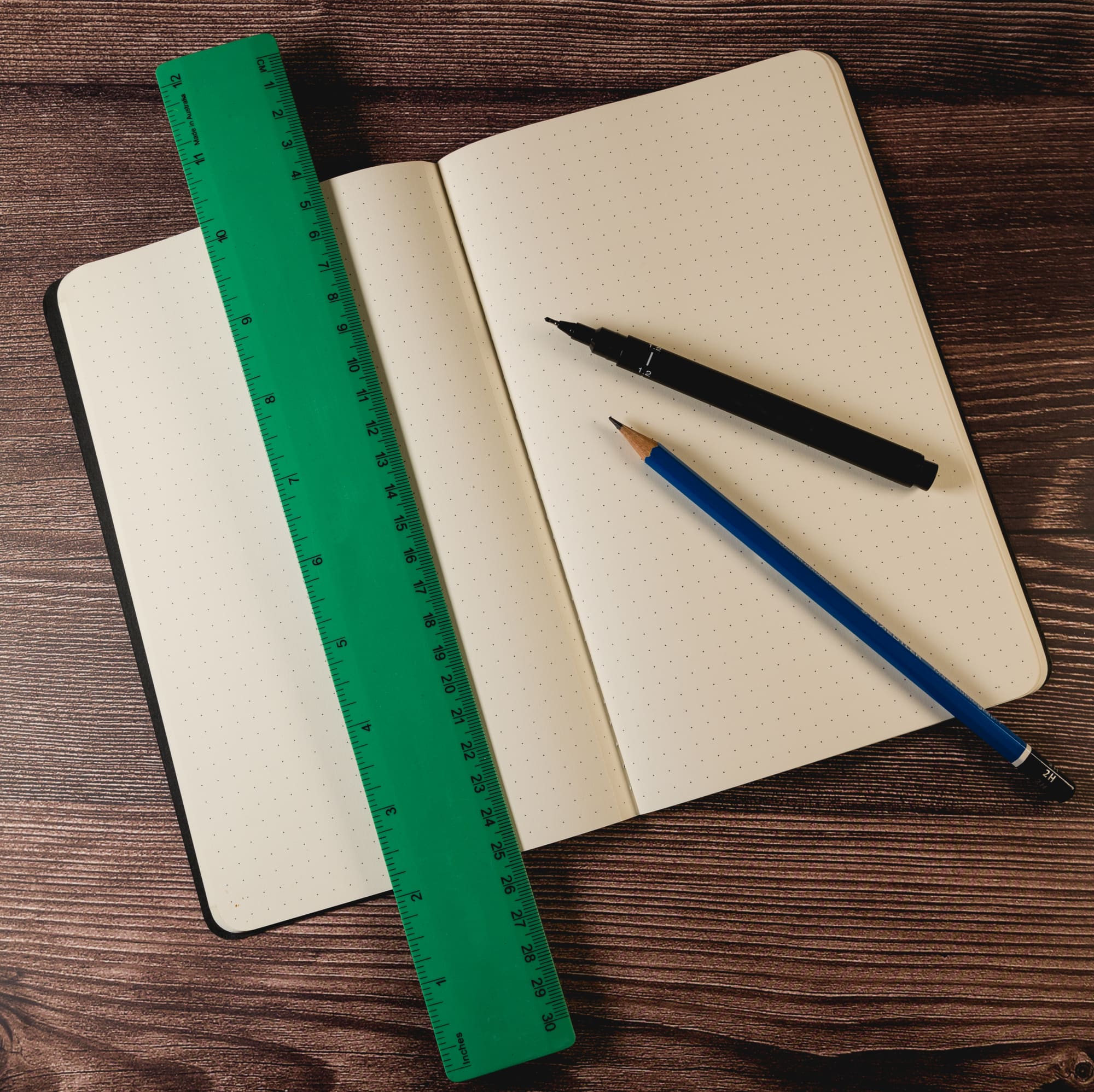A green 30cm recycled plastic ruler next to a black marker and a blue pencil on a dotted notebook.