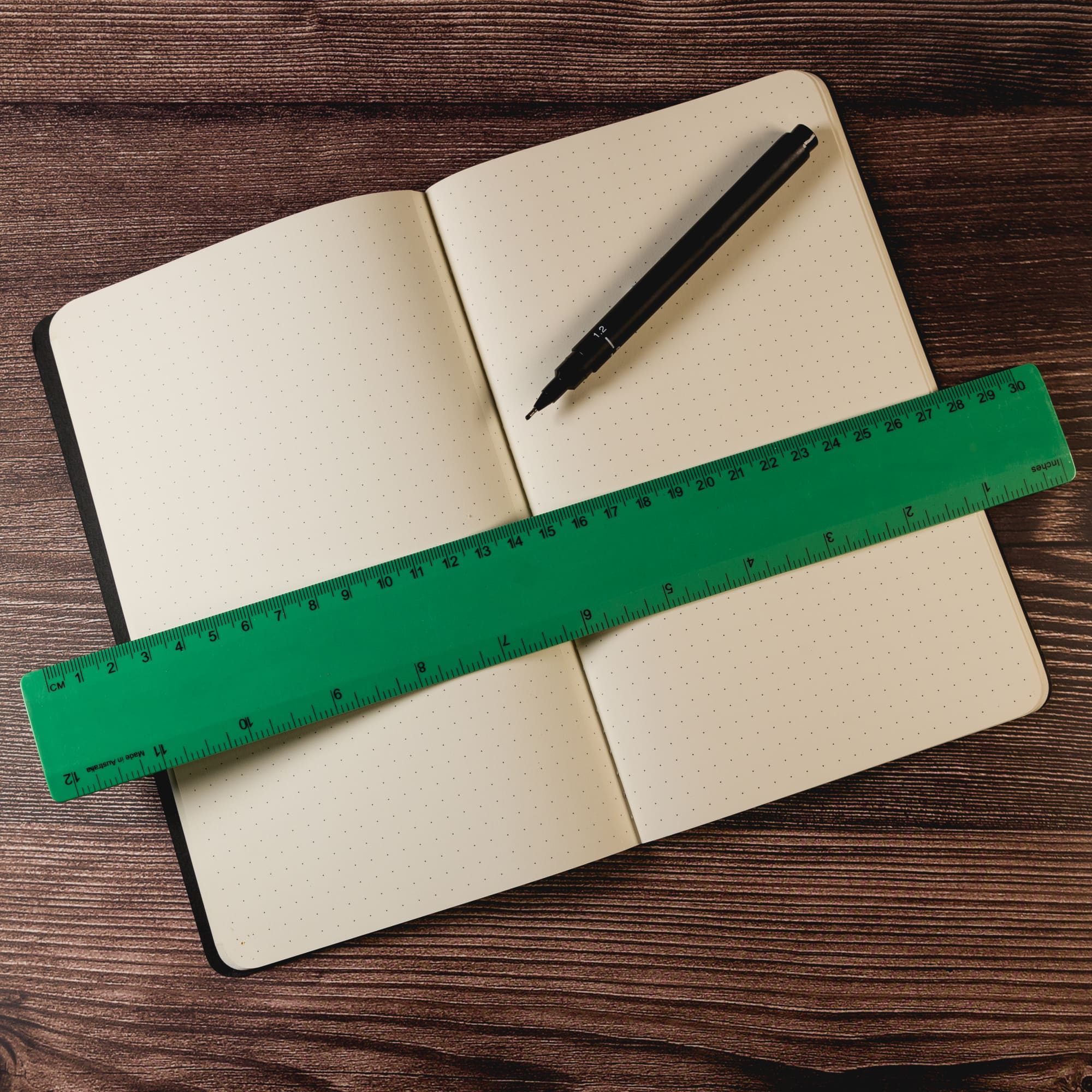 A green recycled plastic ruler measuring 30cm rests across an open dotted notebook and a black pen.