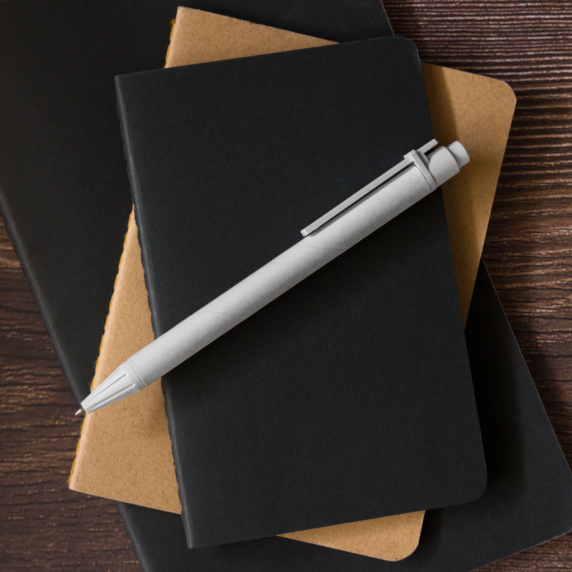 A cardboard pen resting on top of two notebooks, one in black and one in a brown cardboard color.