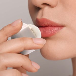 A person applying Ritz Cube Lip Balm to their lips, showcasing the product's sleek packaging and natural lip color.