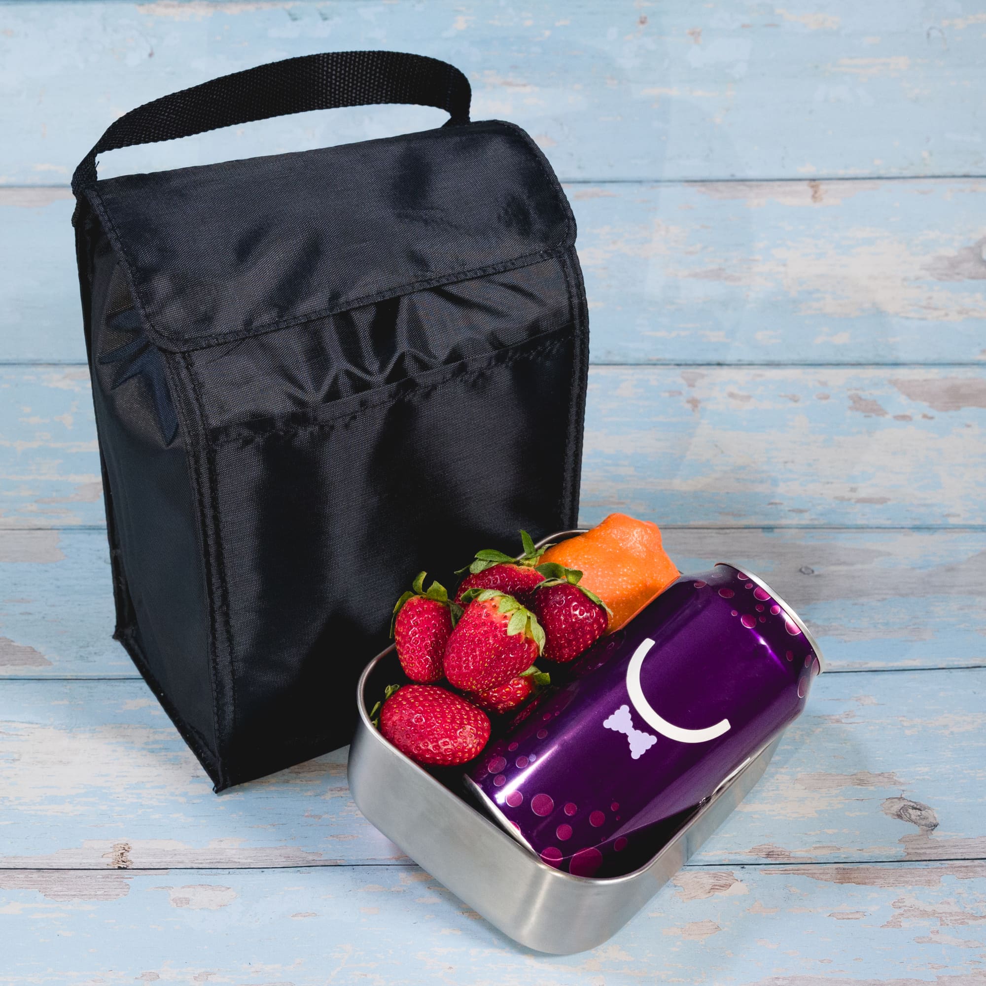 A black cooler lunch bag sits beside a container holding strawberries, a small orange, and a purple drink can.