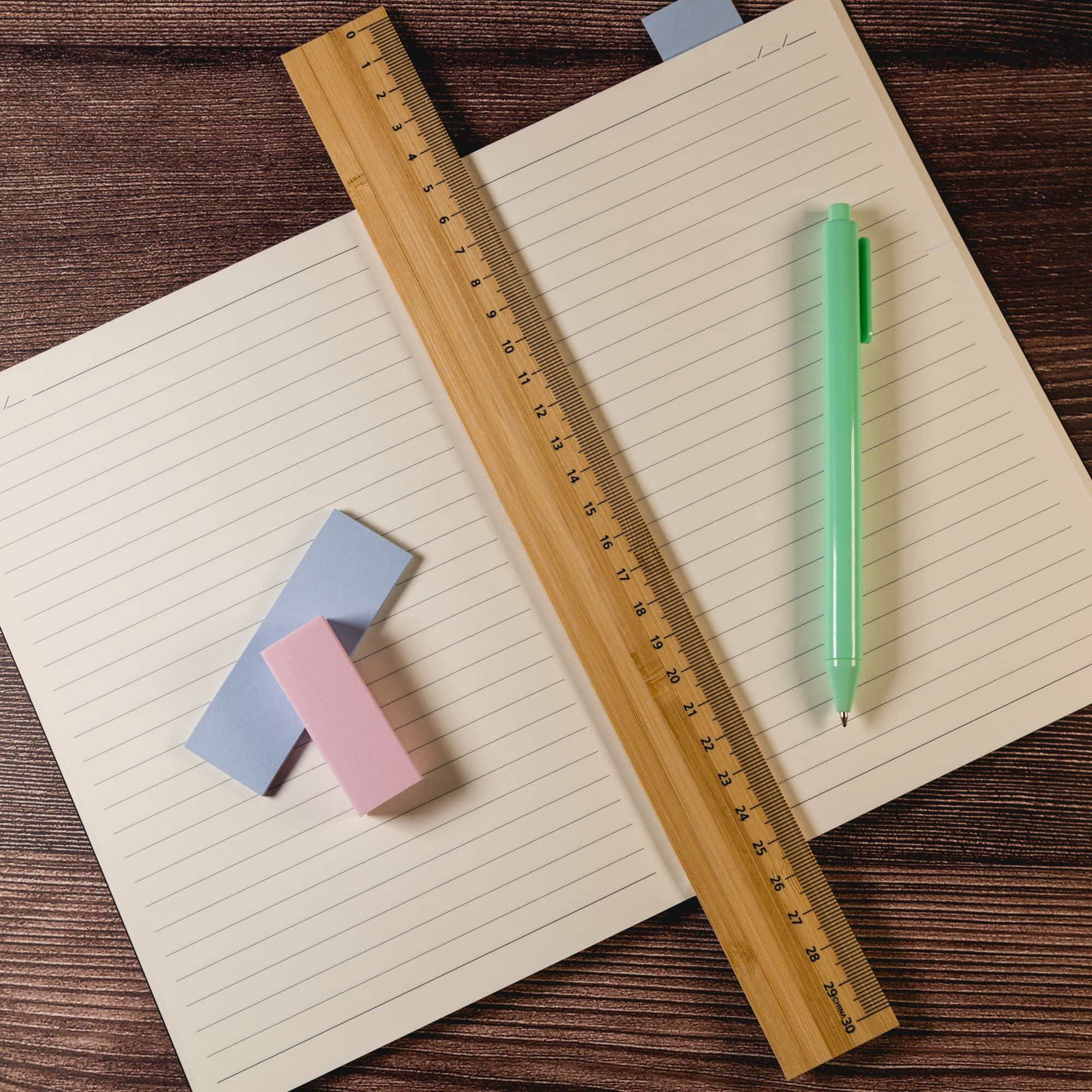 A bamboo 30cm ruler in light brown, placed alongside a green pen and colored sticky notes on a lined notebook.