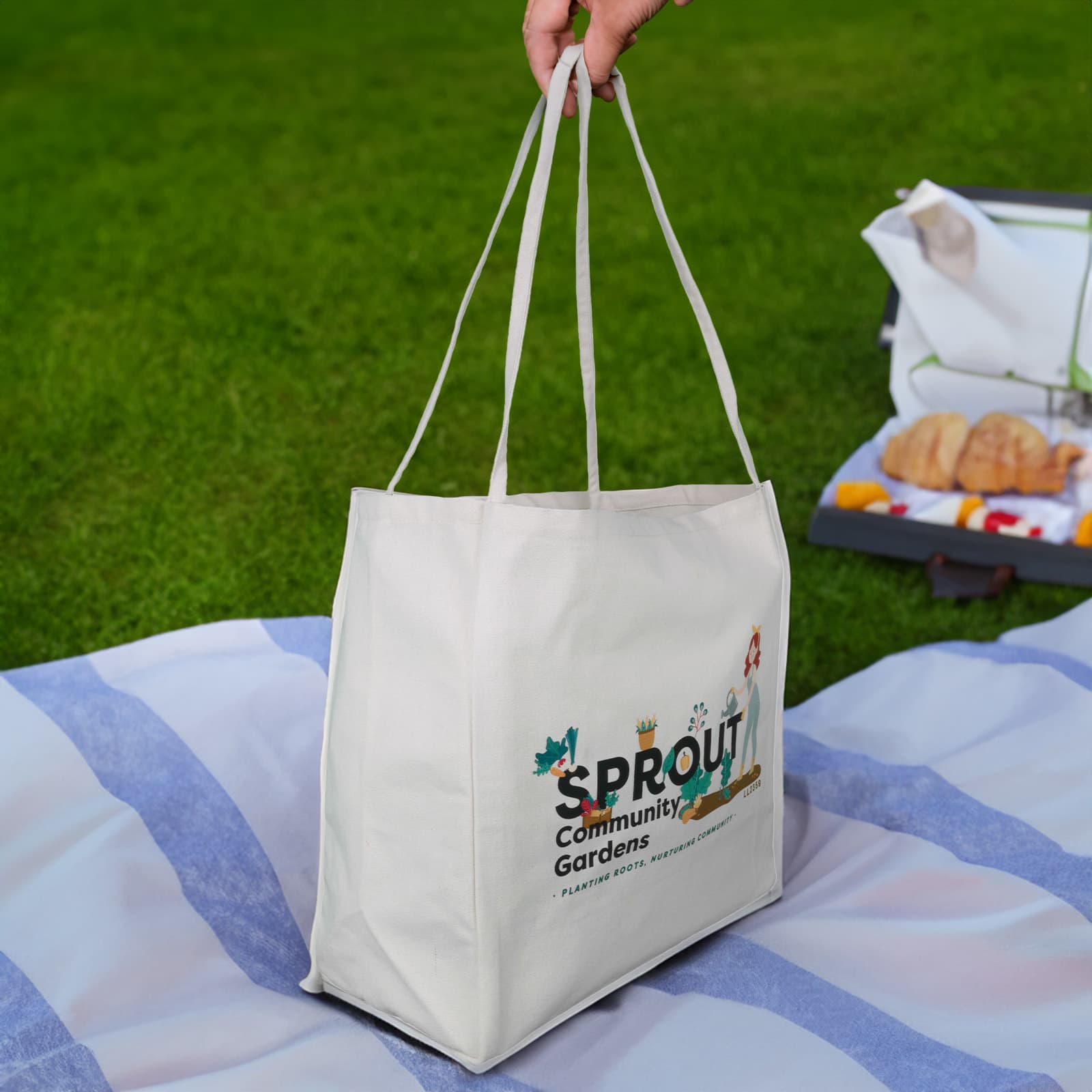 A hand holds a large, cream-coloured tote bag with two long handles and a simple design.