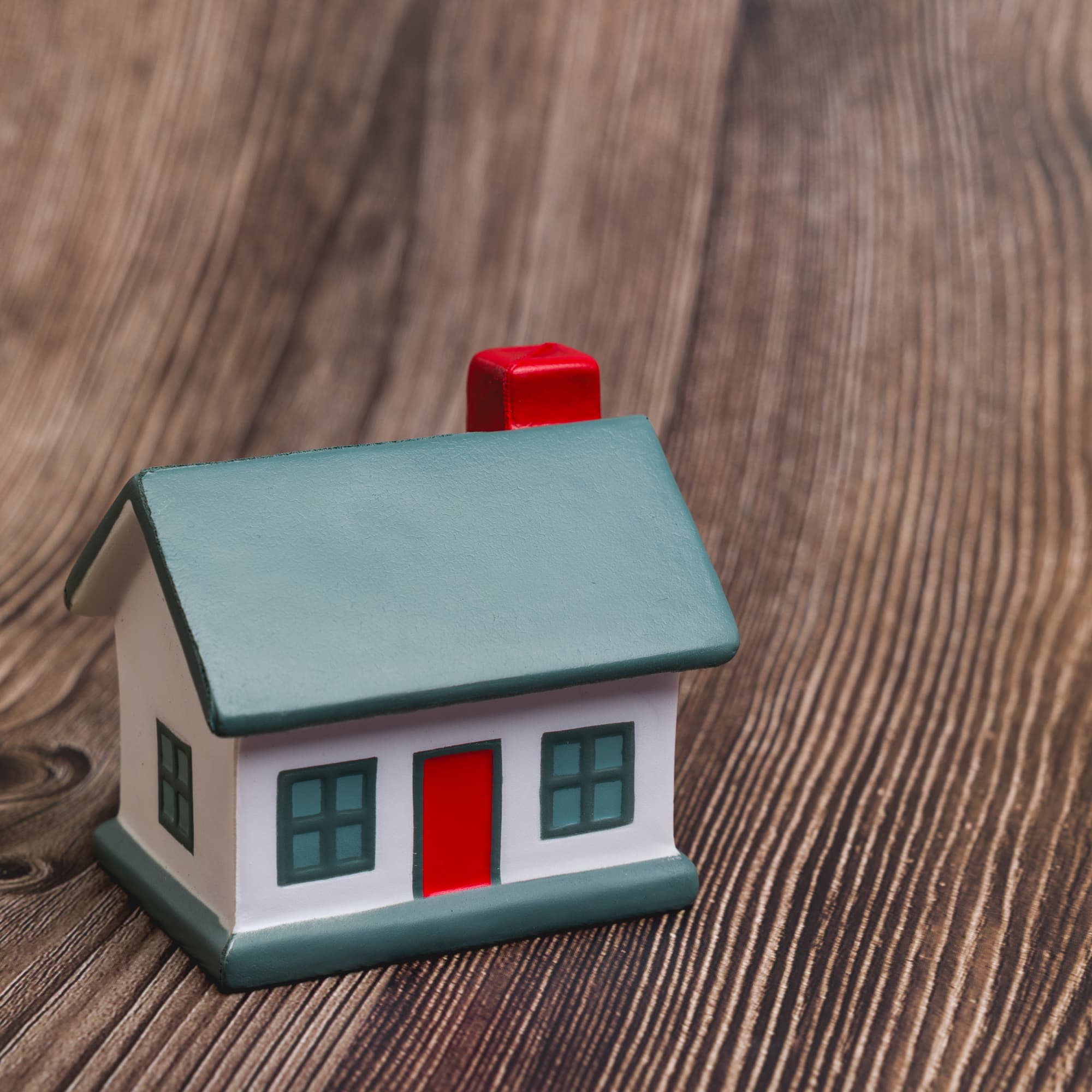 A small, colorful stress-relief house with a green roof, red chimney, and white walls, resting on a wooden surface.