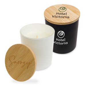 A medium-sized glass candle with a white container, wooden lid, and a black container beside it, both featuring a logo.