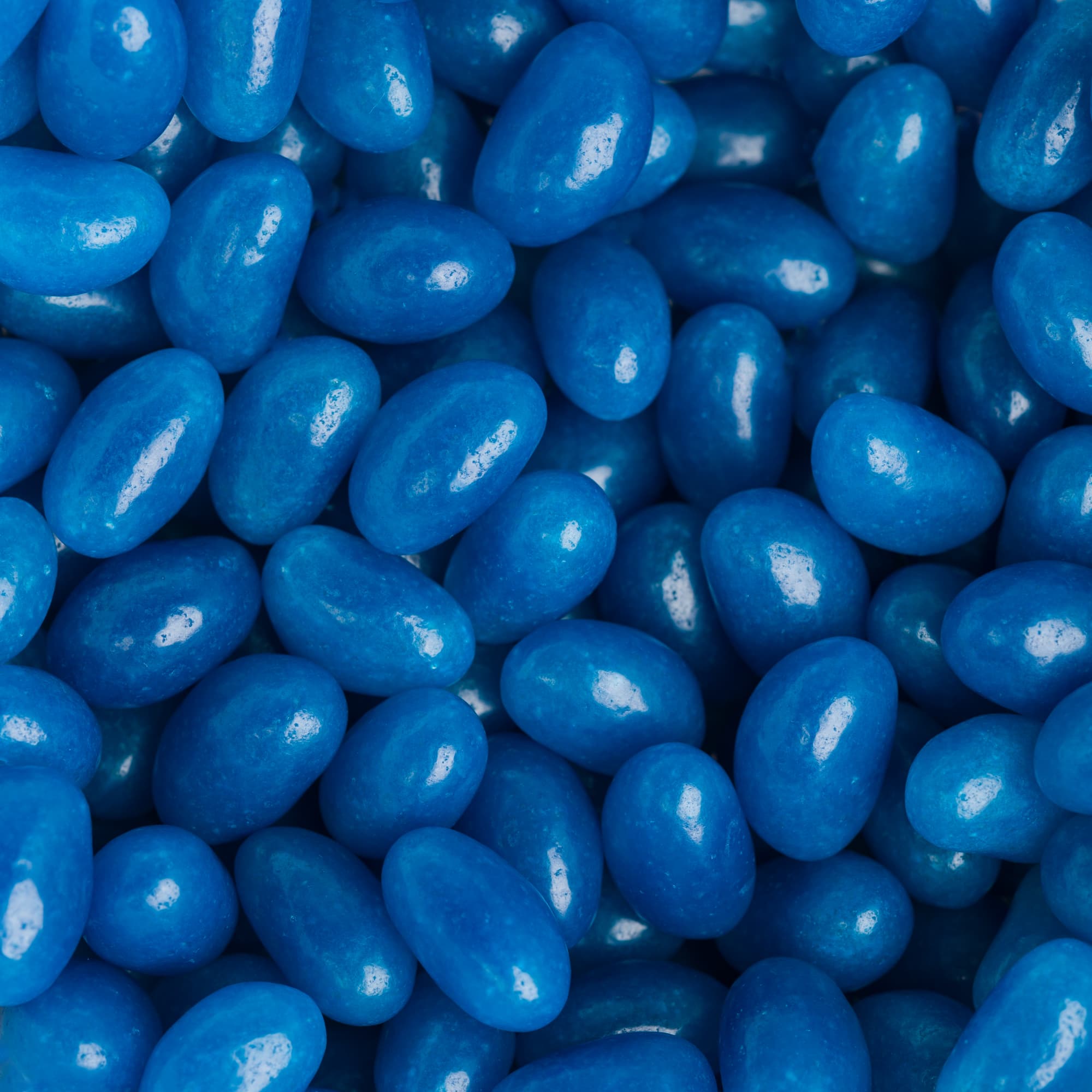 Mini jelly beans in a bright blue color, showcasing a glossy finish and an oval shape, filling the frame.