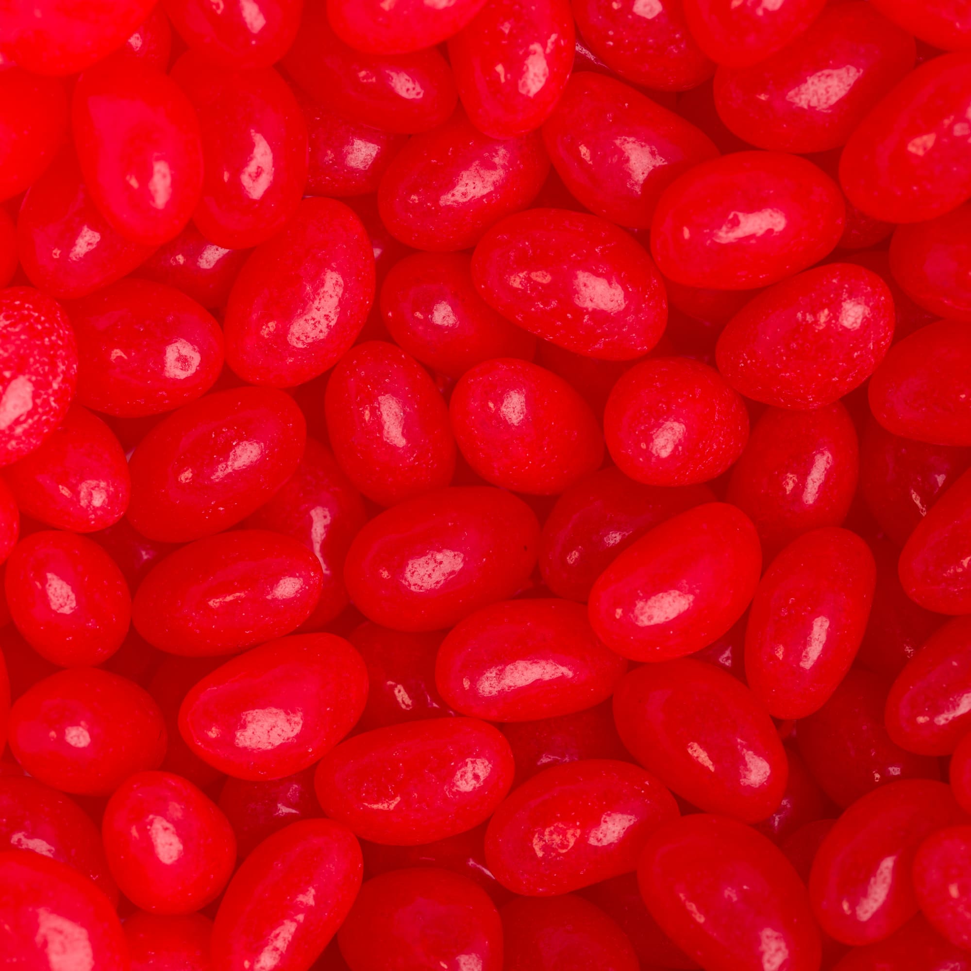 A collection of bright red mini jelly beans in a close-up view, featuring a glossy finish.