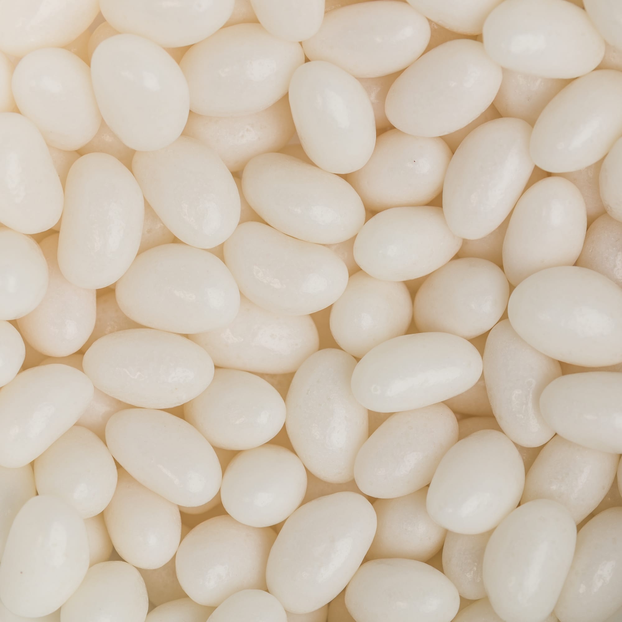 A close-up of white jelly beans, featuring a glossy and smooth surface, scattered closely together.