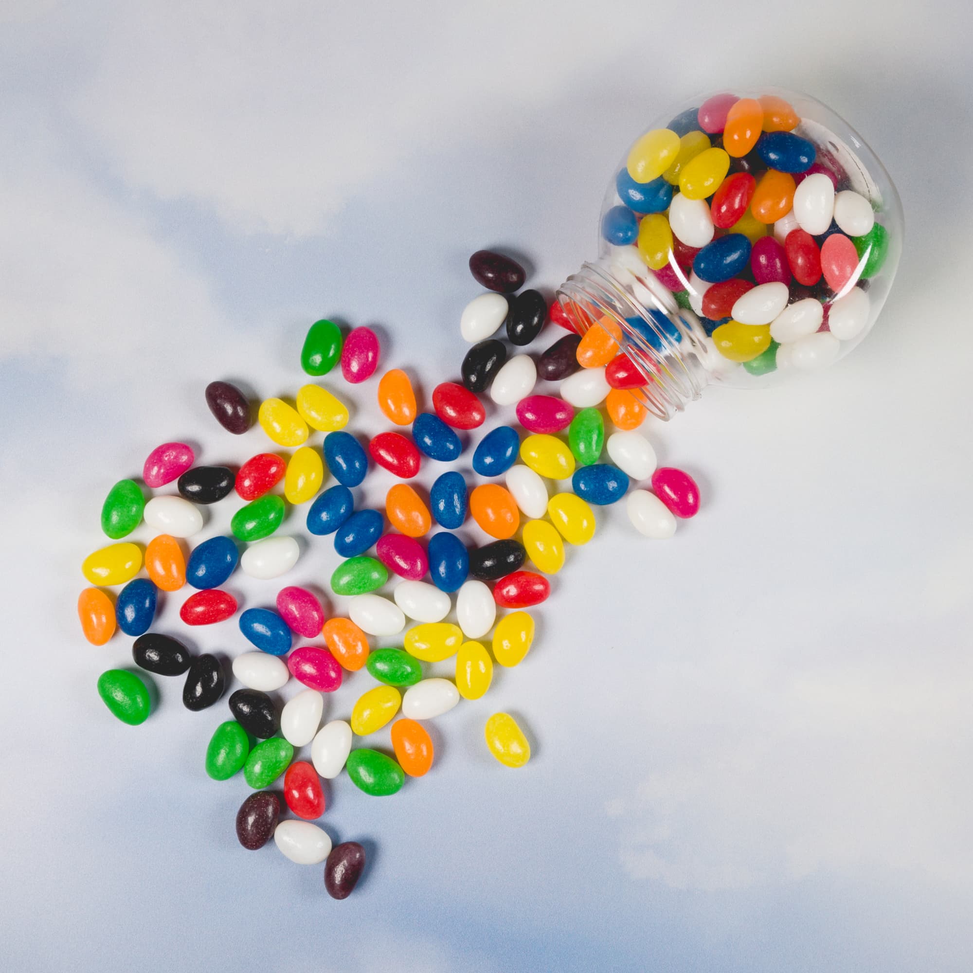 A clear bottle spills an assortment of colourful jelly beans, featuring red, yellow, green, blue, and more.