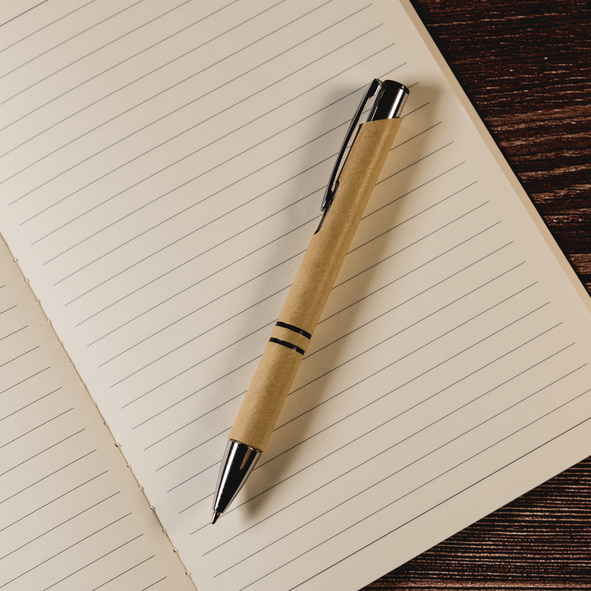 A pen with a natural paper barrel and metallic accents rests on an open lined notebook.