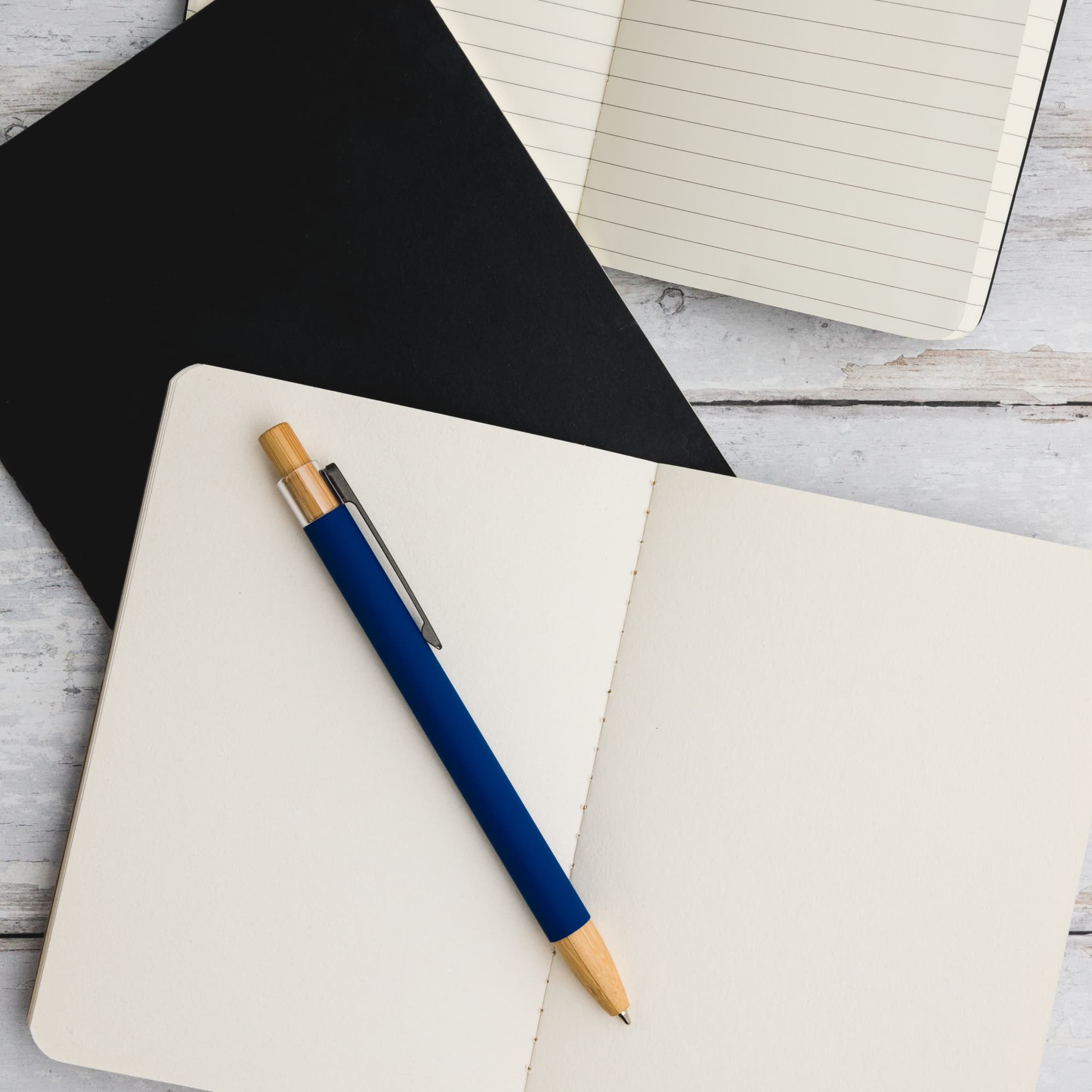 A Serenity Aluminium Pen rests on an open notebook with blank pages, accompanied by a black notebook in the background.