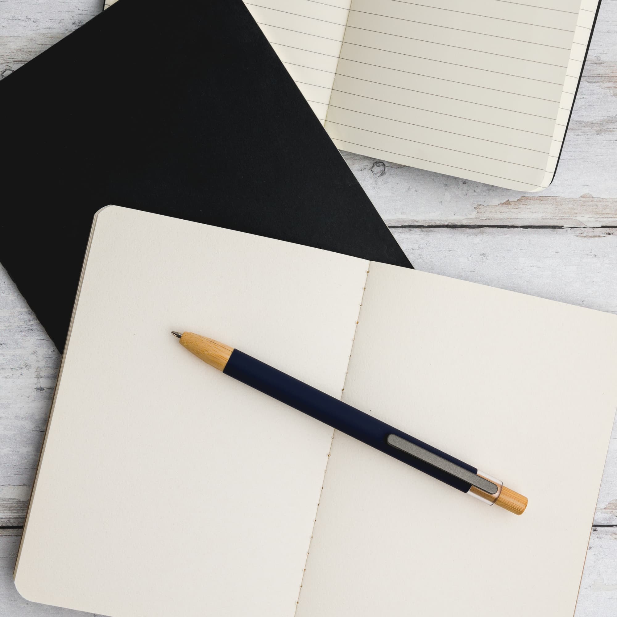 A metal pen with a blue barrel and wooden accents resting on an open notebook with blank pages.