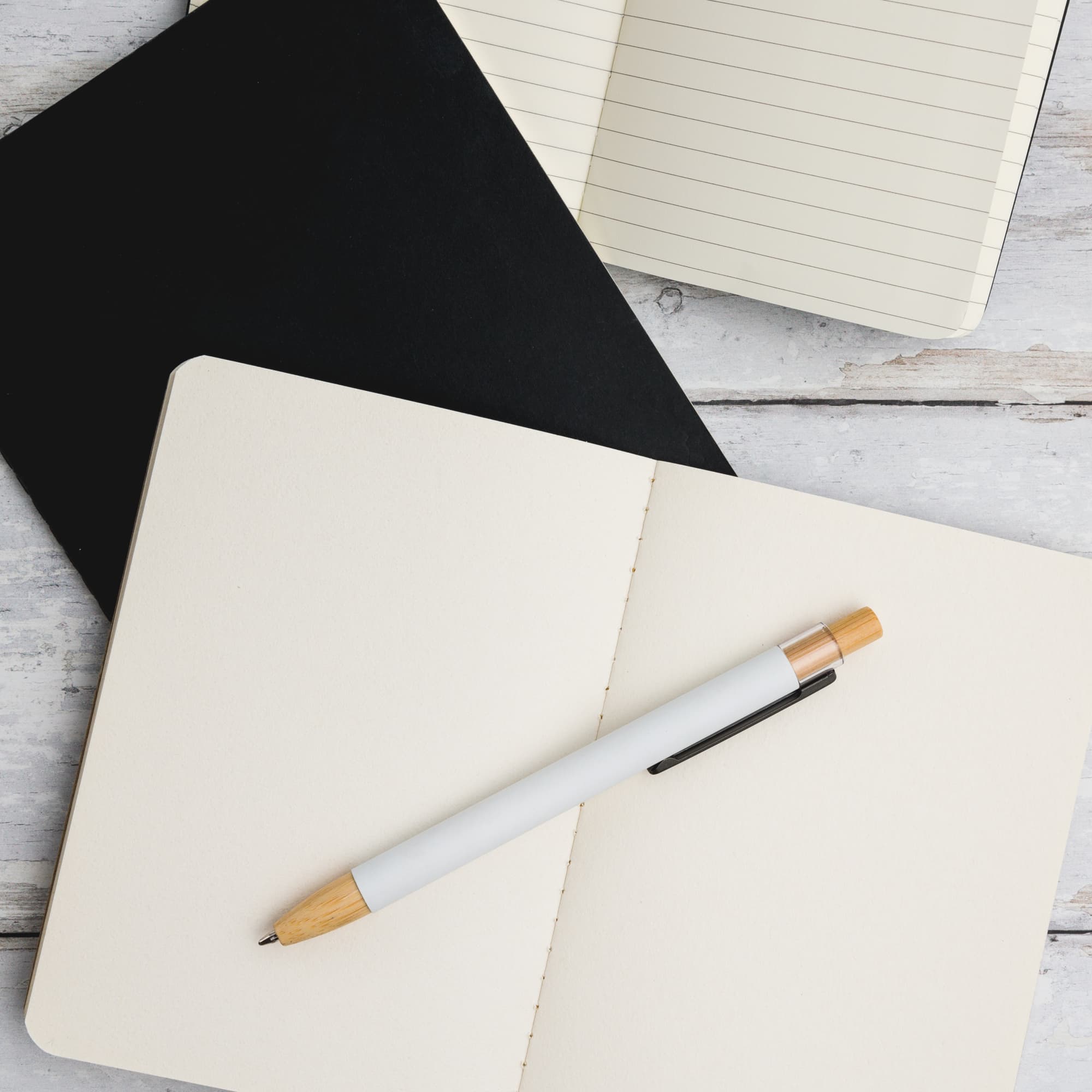 A white aluminium pen with a wooden accent rests on an open, blank notebook on a wooden surface.