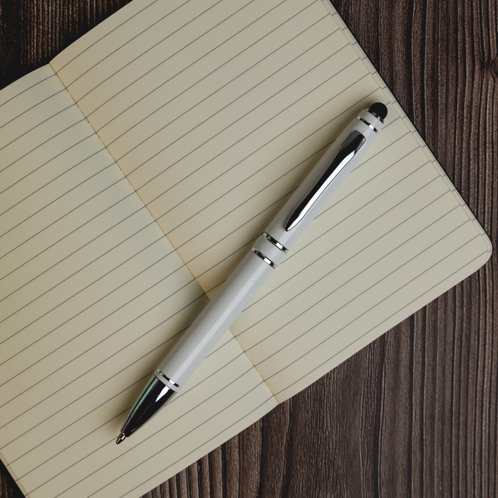 A metal pen in silver and black rests on a lined notebook page. The pen features a sleek design and a branding logo.