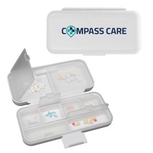 A white compact pill organizer with multiple compartments and a transparent lid, featuring a logo on top.