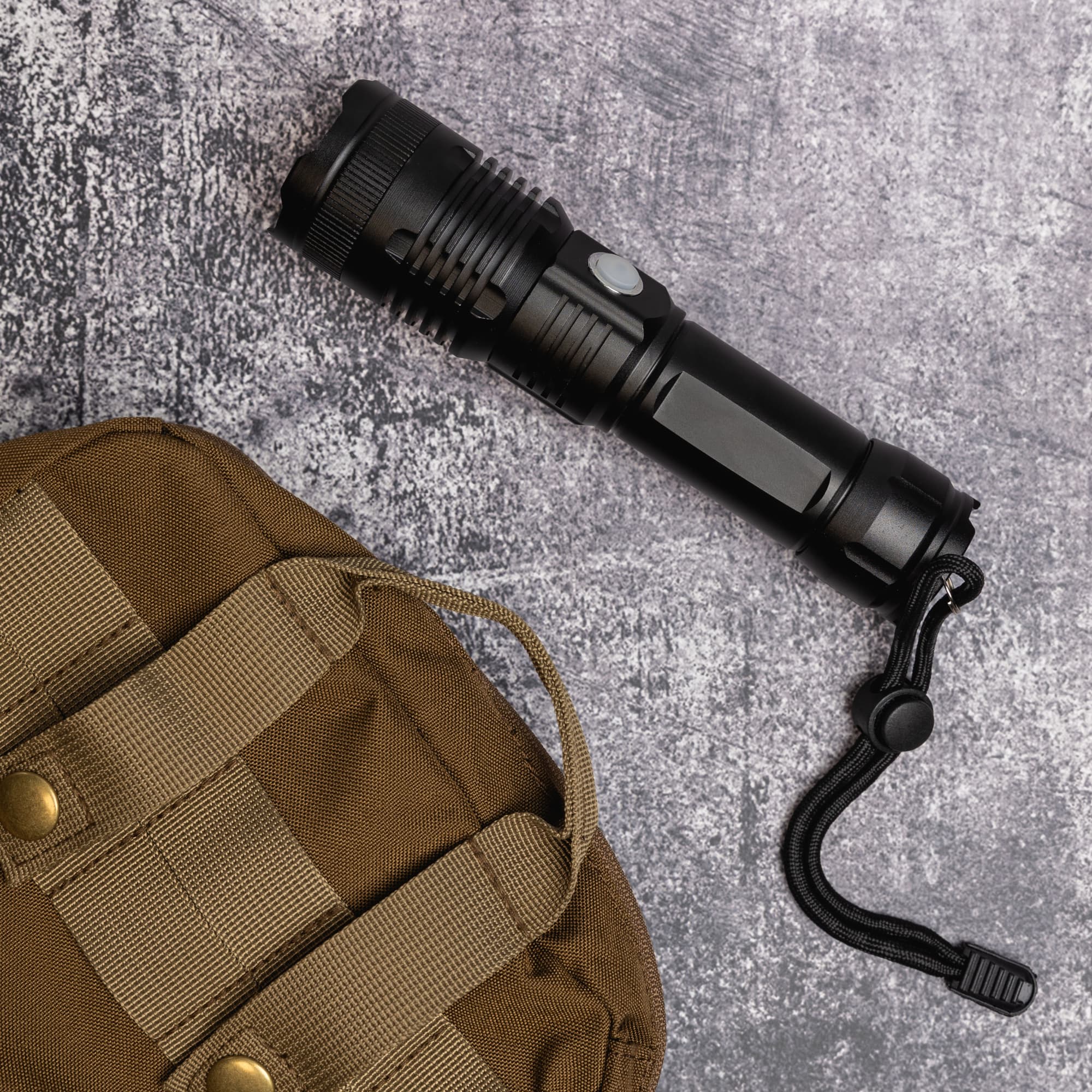 A rechargeable torch lies beside a brown bag, featuring a sleek black design with a button for operation.