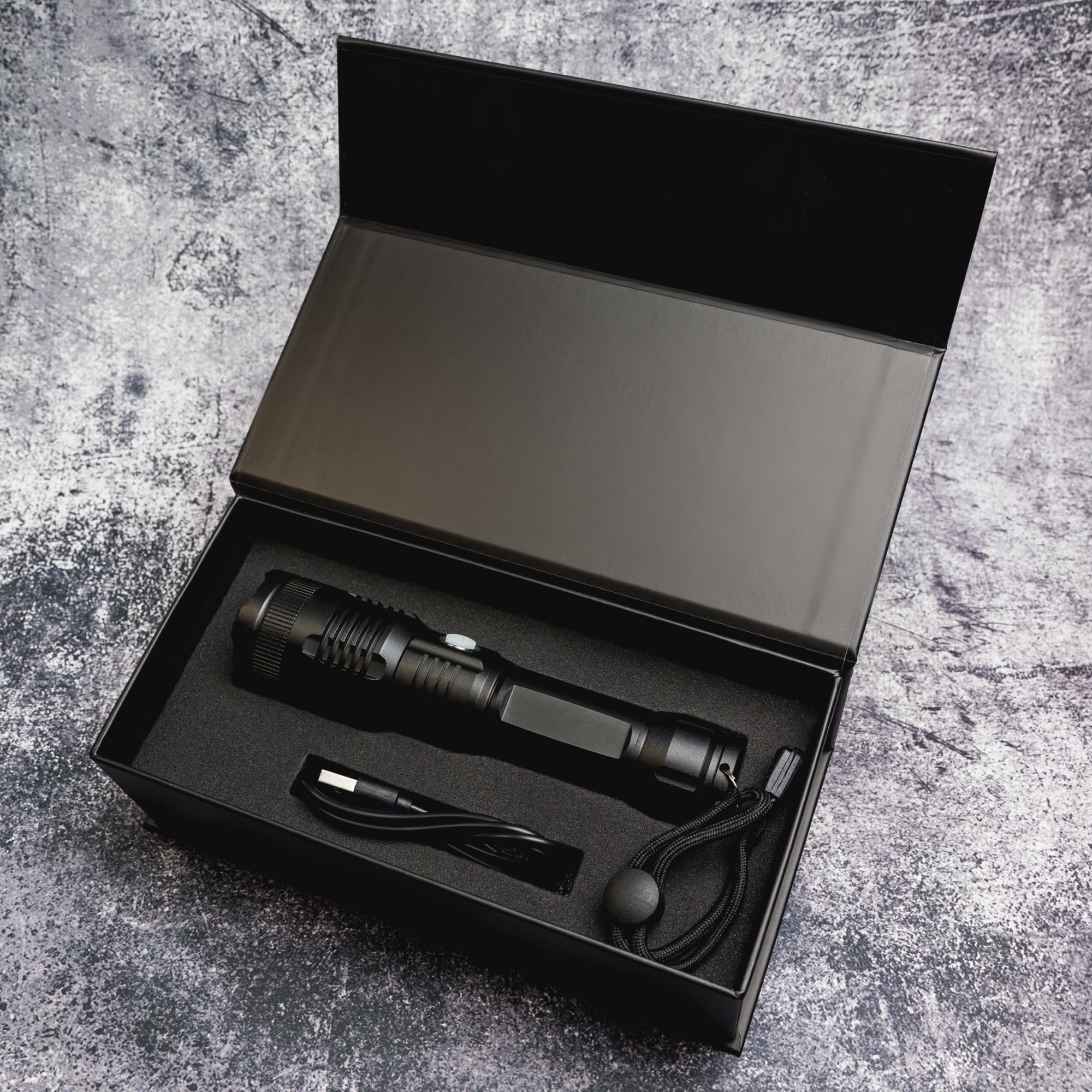 A rechargeable torch in a sleek black box, accompanied by a charging cable and a lanyard.