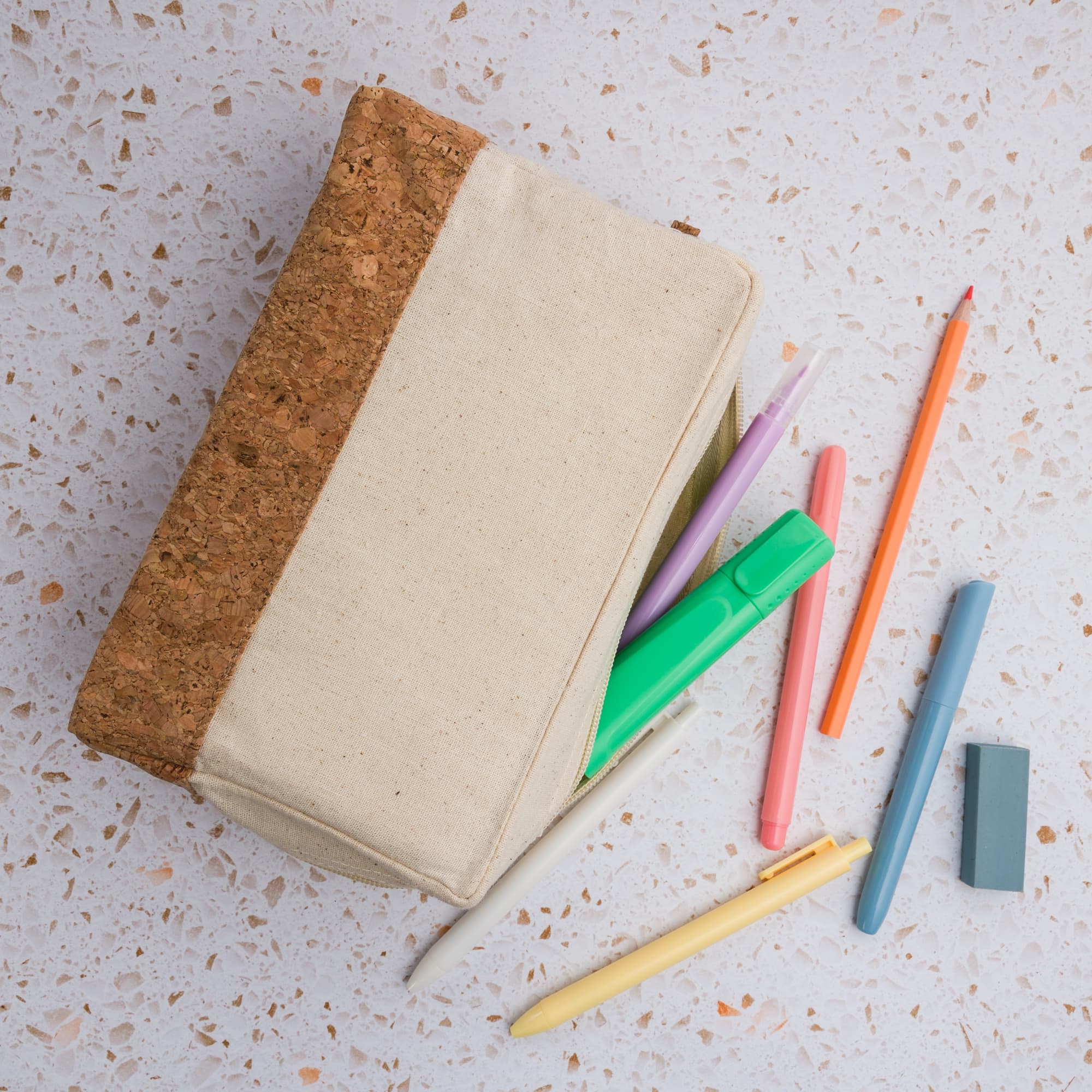 A cork and beige utility case with colorful pens and markers nearby. The case features a textured cork side.