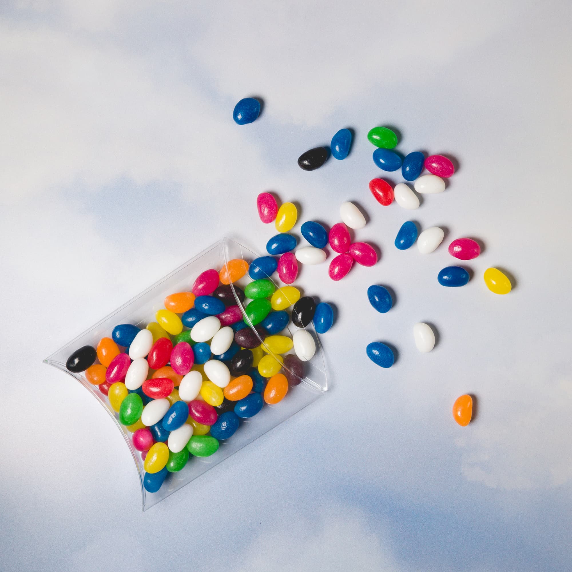 Assorted Colour Mini Jelly Beans in a clear pillow pack, with colorful jelly beans scattered around.