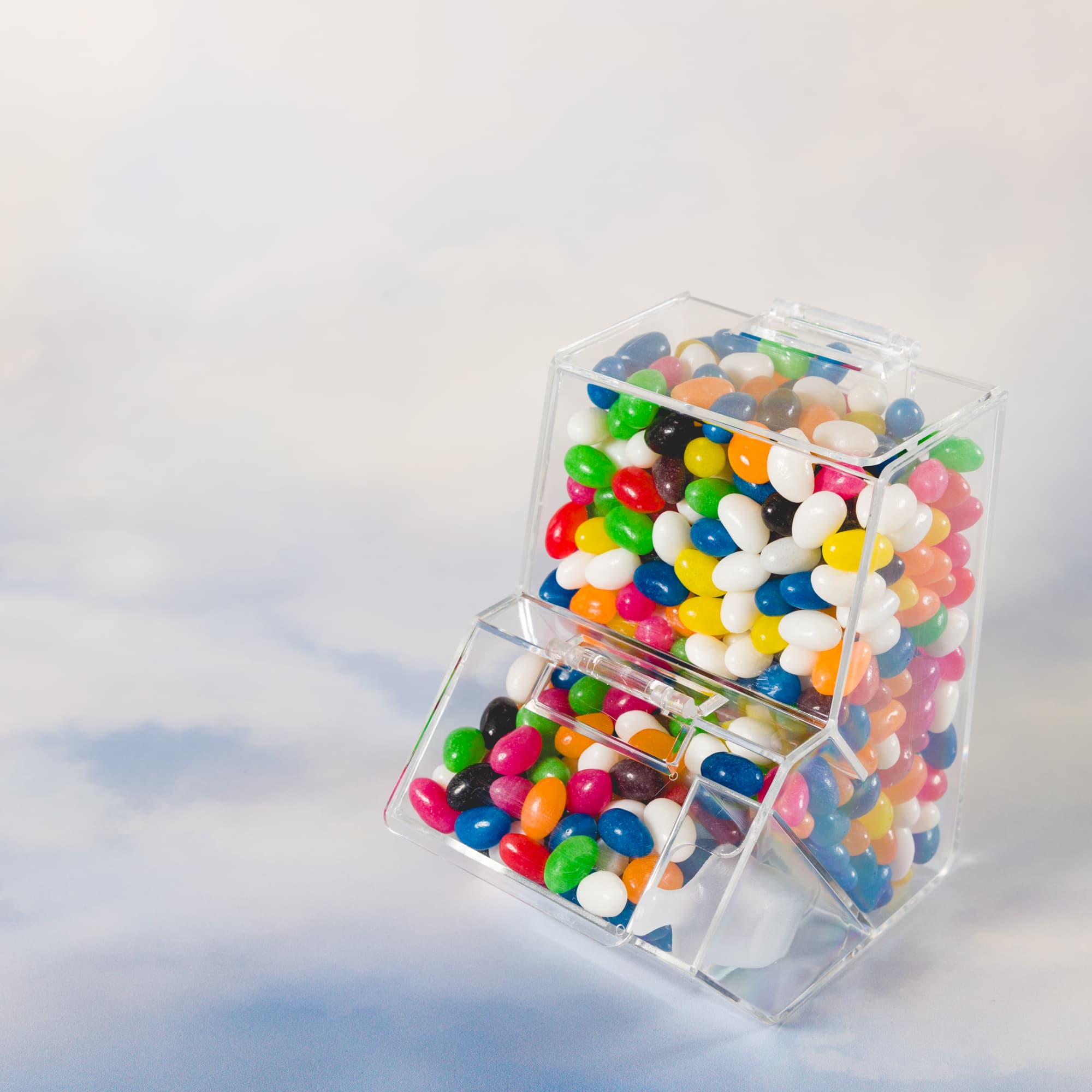 A clear dispenser filled with assorted color mini jelly beans in various shades, including red, blue, green, and white.