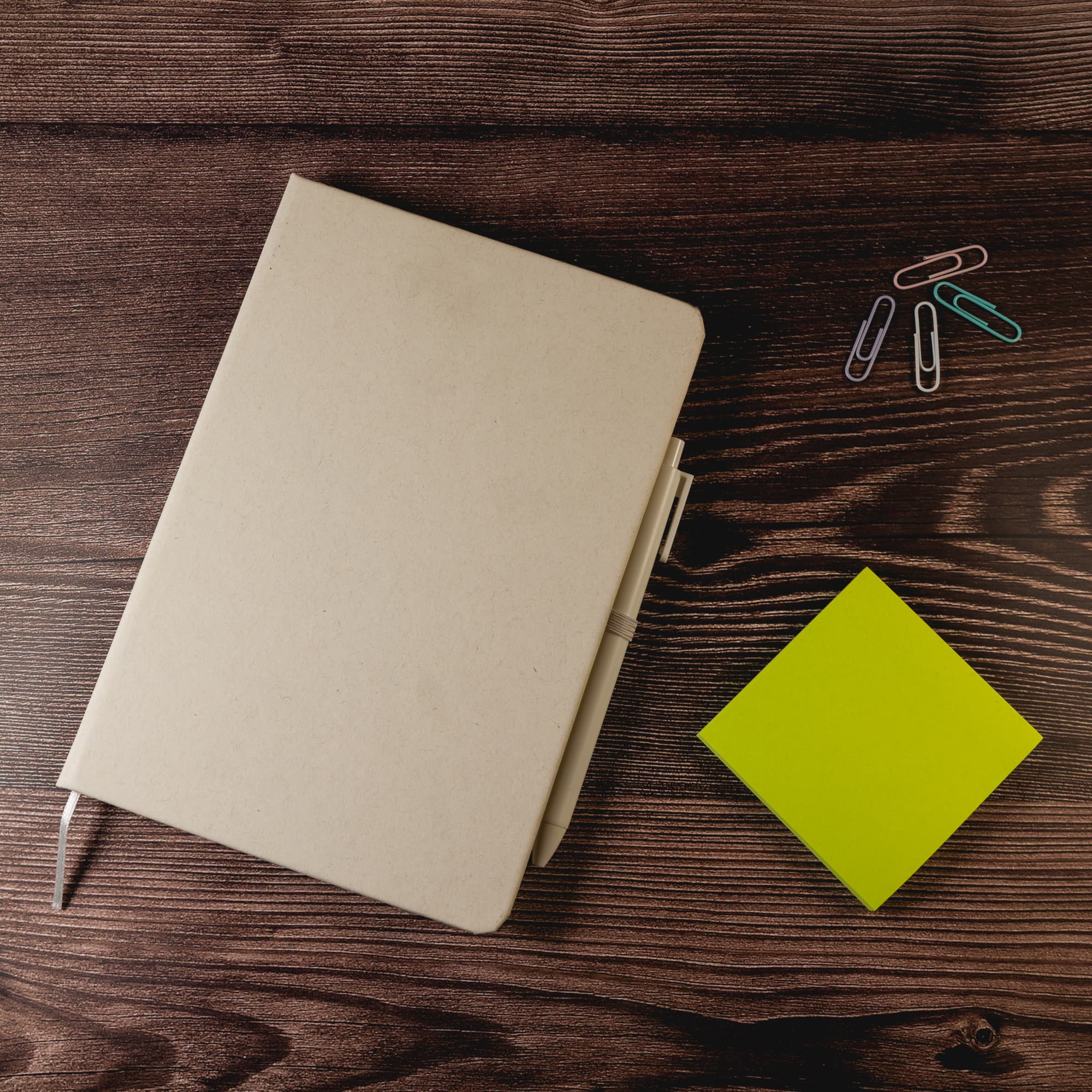A Venture Snowy A5 Notebook in a neutral color, accompanied by a green sticky note and colorful paper clips.