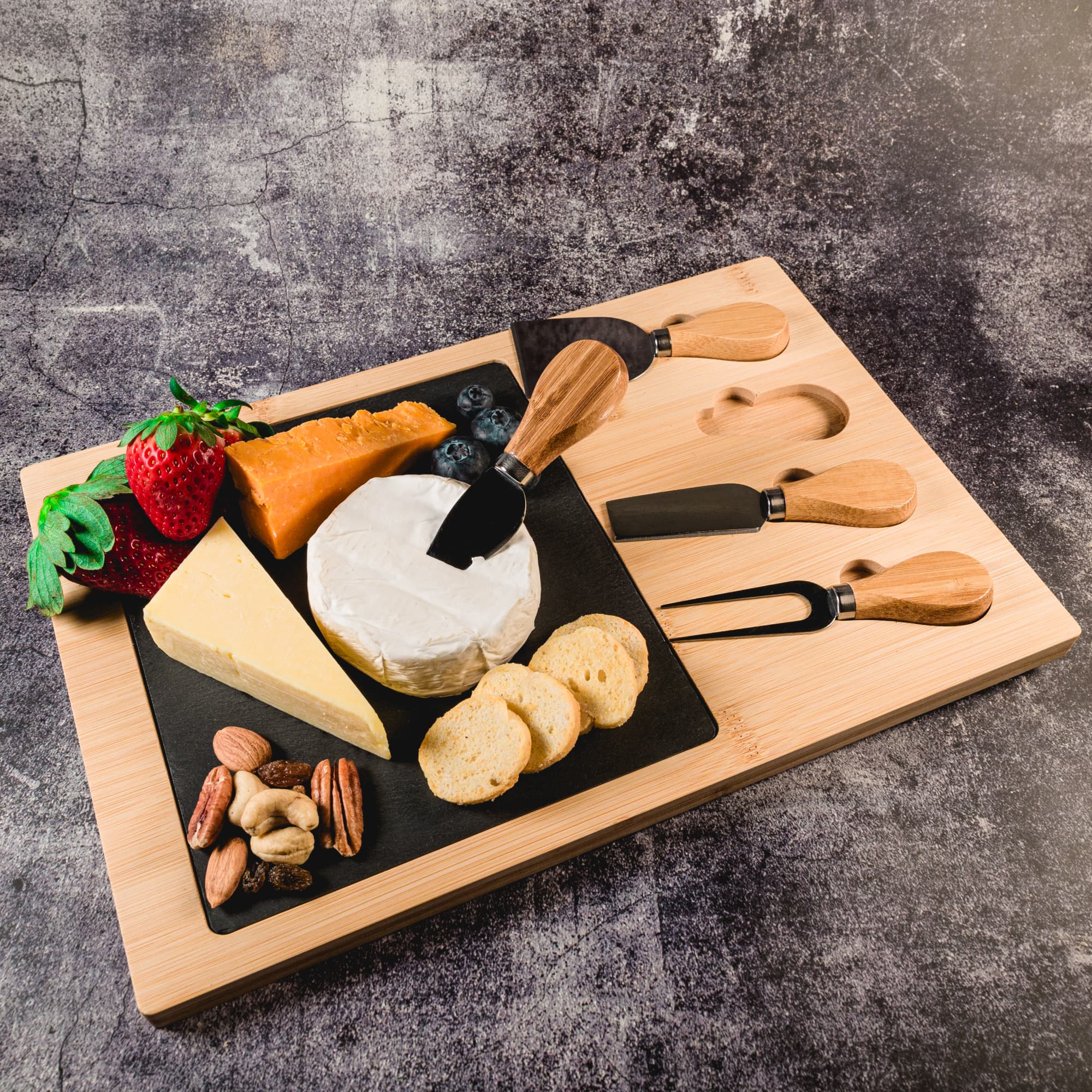 A Bamboo Slate Cheese Board featuring a variety of cheeses, fresh fruits, and nuts, accompanied by cheese knives.