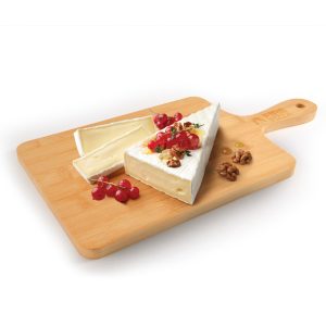 A bamboo serving board featuring a wedge of cheese topped with red currants, nuts, and herbs.