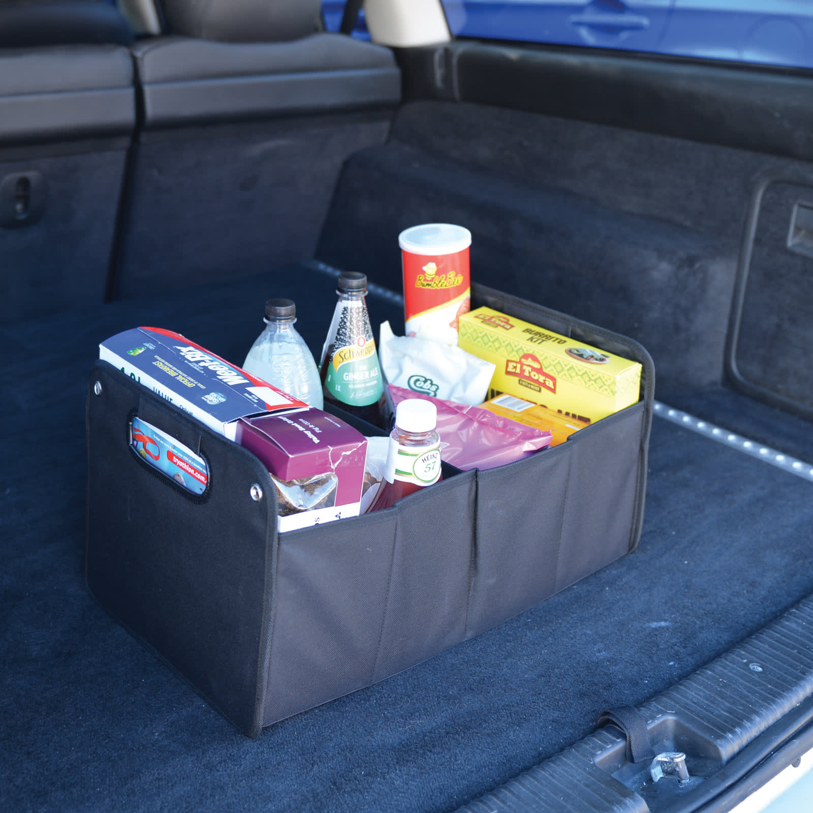 A black storage organizer filled with drinks and snacks, displayed in the trunk of a vehicle.