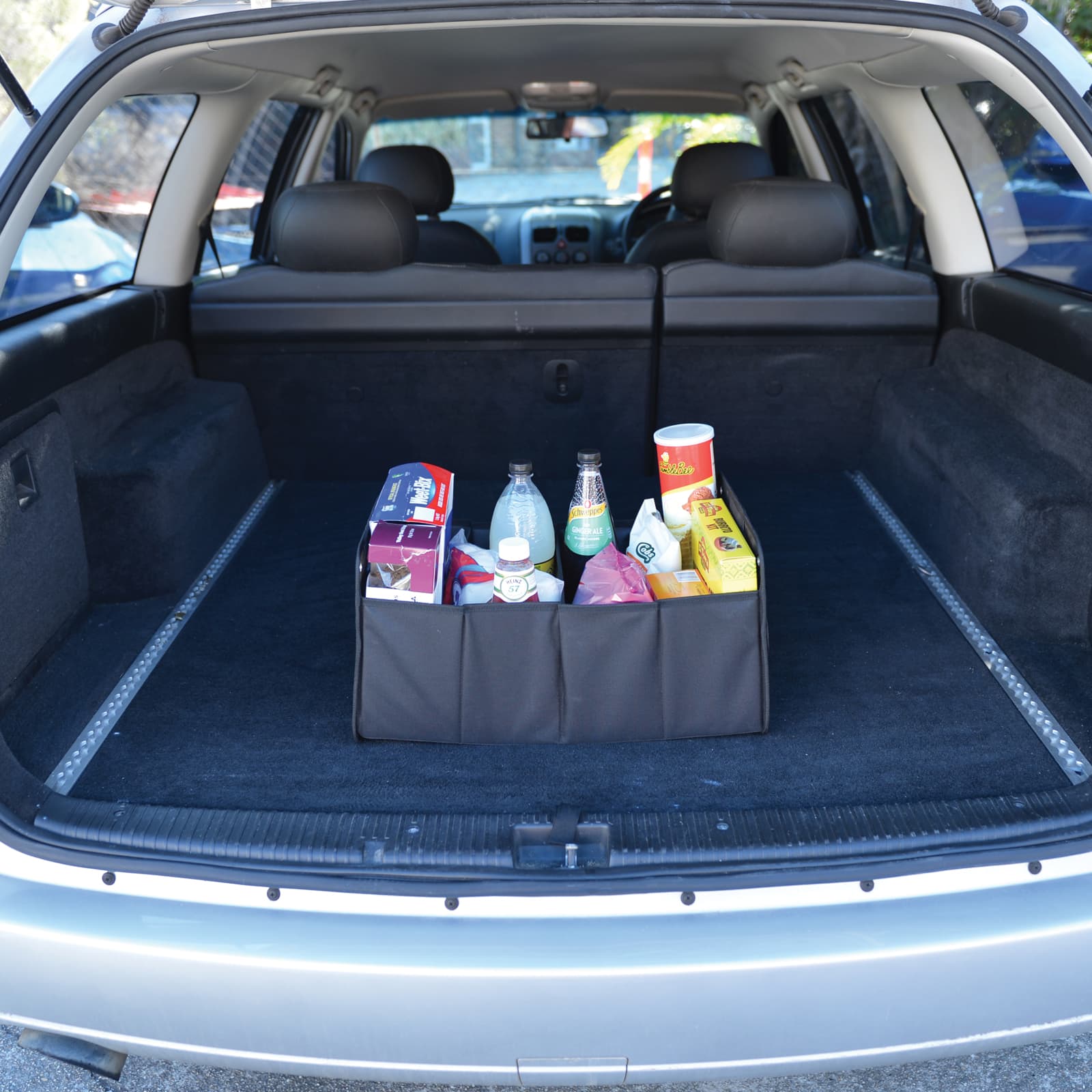 A black cargo storage organiser filled with various drink bottles and snacks, placed in the trunk of a car.