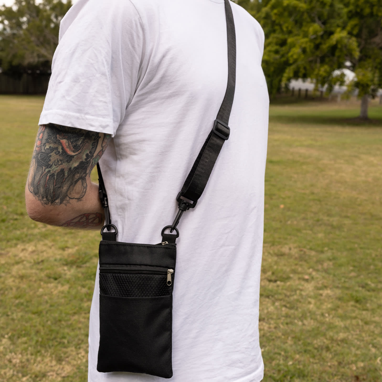 A black Wallaby Neck Pouch hangs from a person's shoulder, featuring a zippered pocket and adjustable strap.
