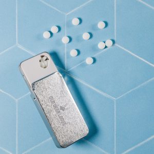 A silver slider tin containing sugar-free breath mints, with white mints scattered beside it on a pastel blue background.