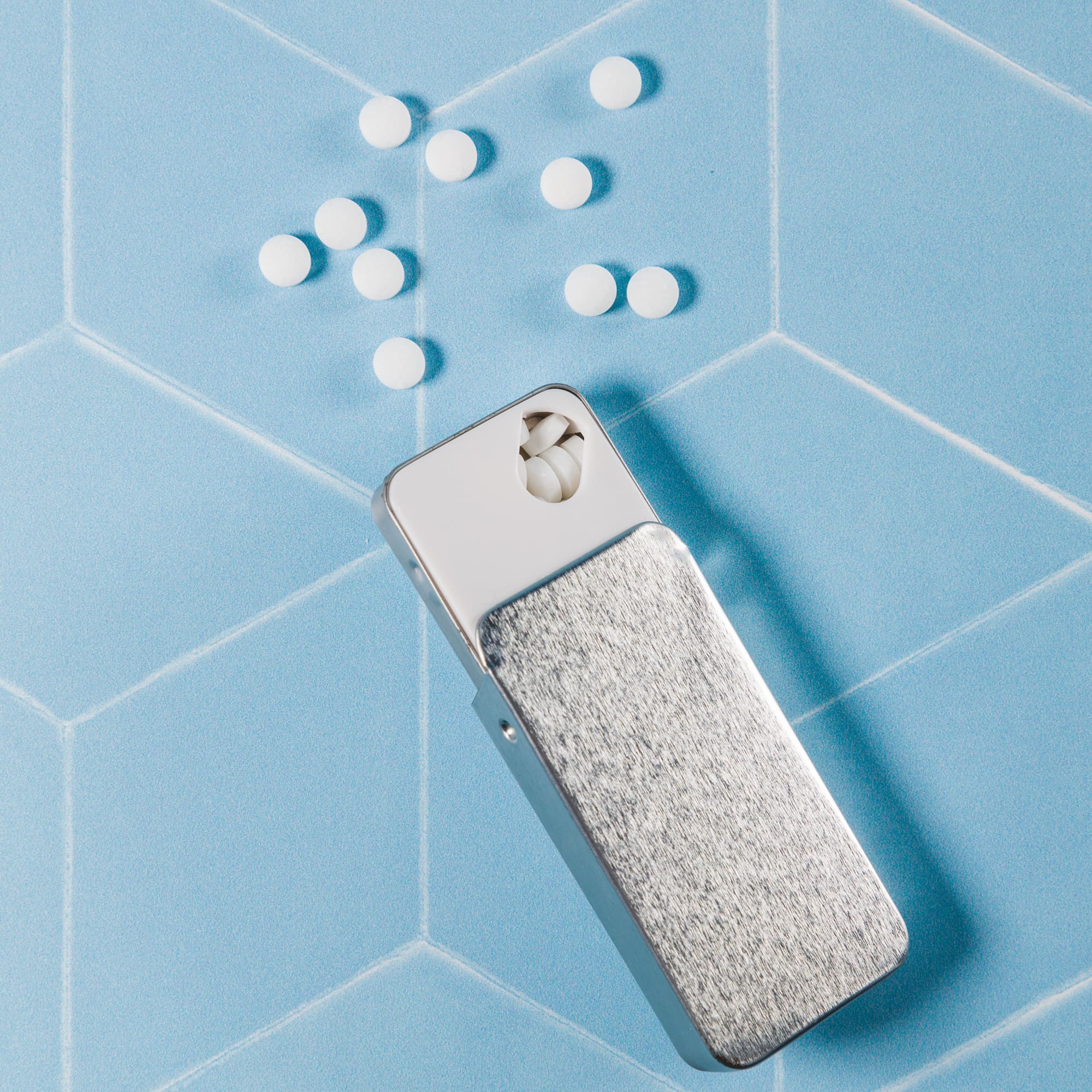 A silver slider tin containing sugar-free breath mints, with a few mints visible outside.