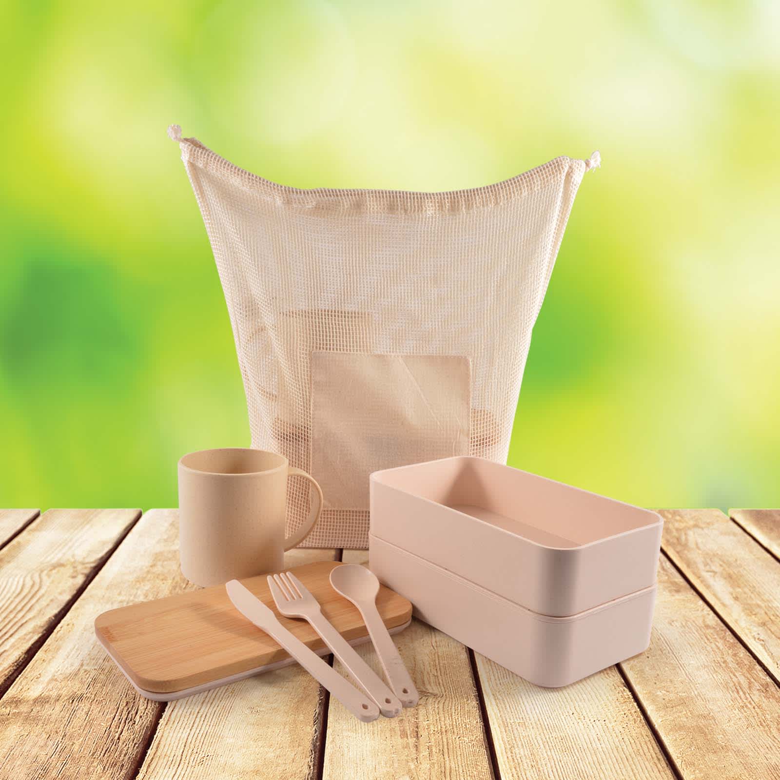 A light beige eco-friendly pack containing containers, utensils, and a cup, arranged on a wooden surface with a green background.